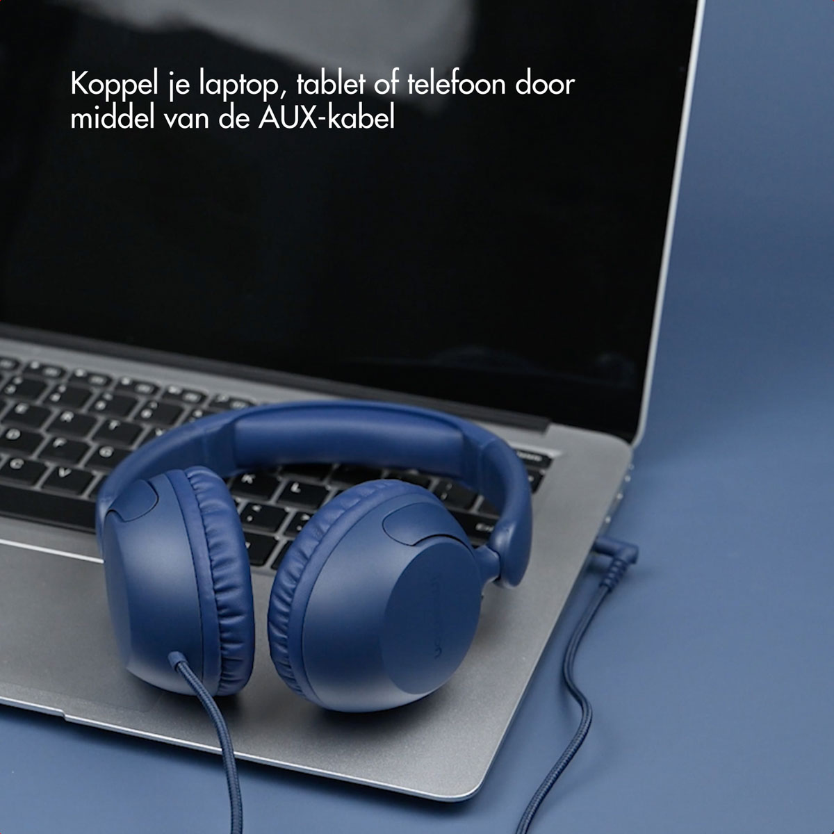 Blue headphones are connected to a laptop via a cable. The laptop is on a blue surface.