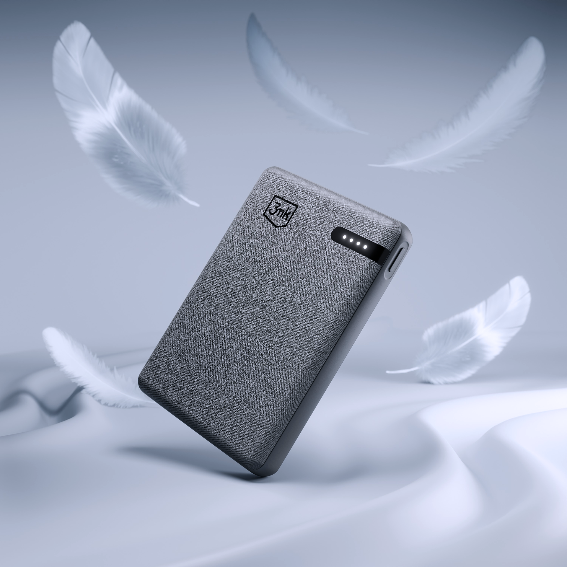 Szary power bank, otoczony unoszącymi się białymi piórami. Ma teksturowaną powierzchnię i kontrolki na białym tle.