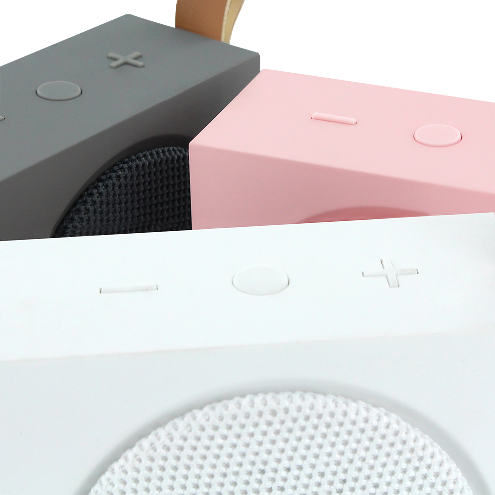 Primer plano de tres altavoces en gris, rosa y blanco. Botones arriba y malla.