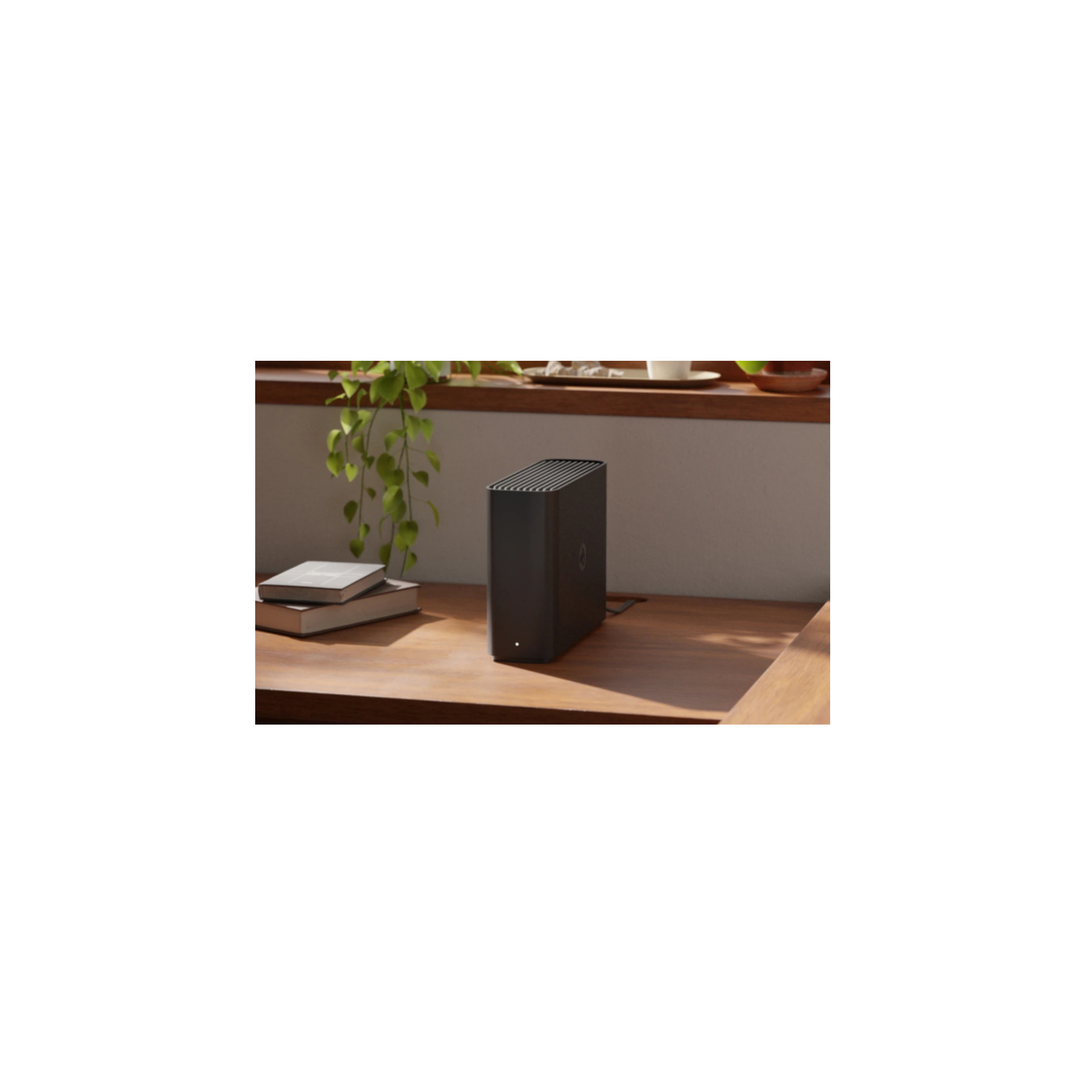 Un appareil noir est posé sur une table en bois. Il y a une fenêtre et des plantes en arrière-plan.
