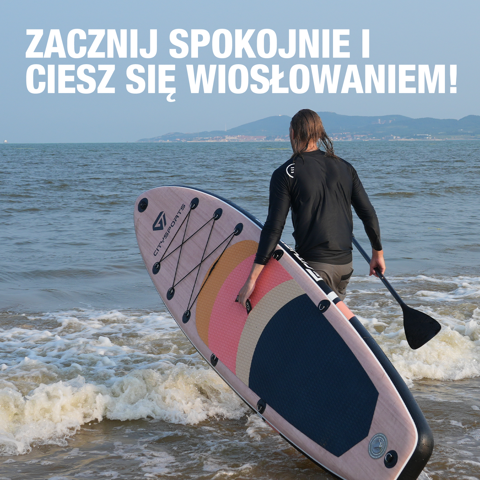 Mężczyzna na desce SUP na oceanie, trzymający wiosło. Woda jest falista, a w oddali widać góry.
