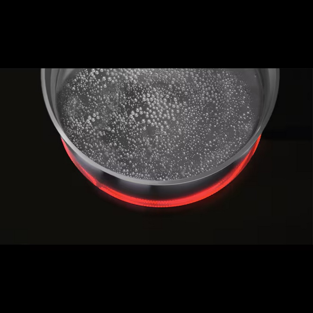 Una pentola di vetro con acqua bollente su un fornello rosso incandescente. Le bolle salgono nell'acqua. Lo sfondo è nero.
