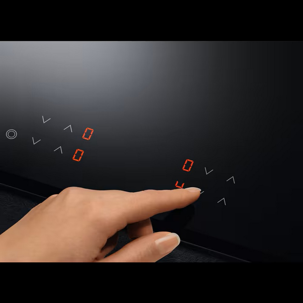 Una mano che tocca i numeri su un piano cottura a induzione nero.