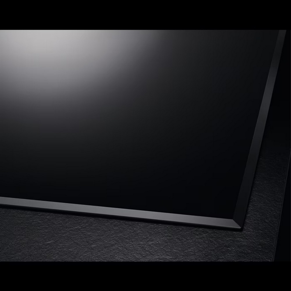 Primo piano di un piano cottura in vetroceramica nero. Ha una superficie liscia e riflettente e un bordo scuro.