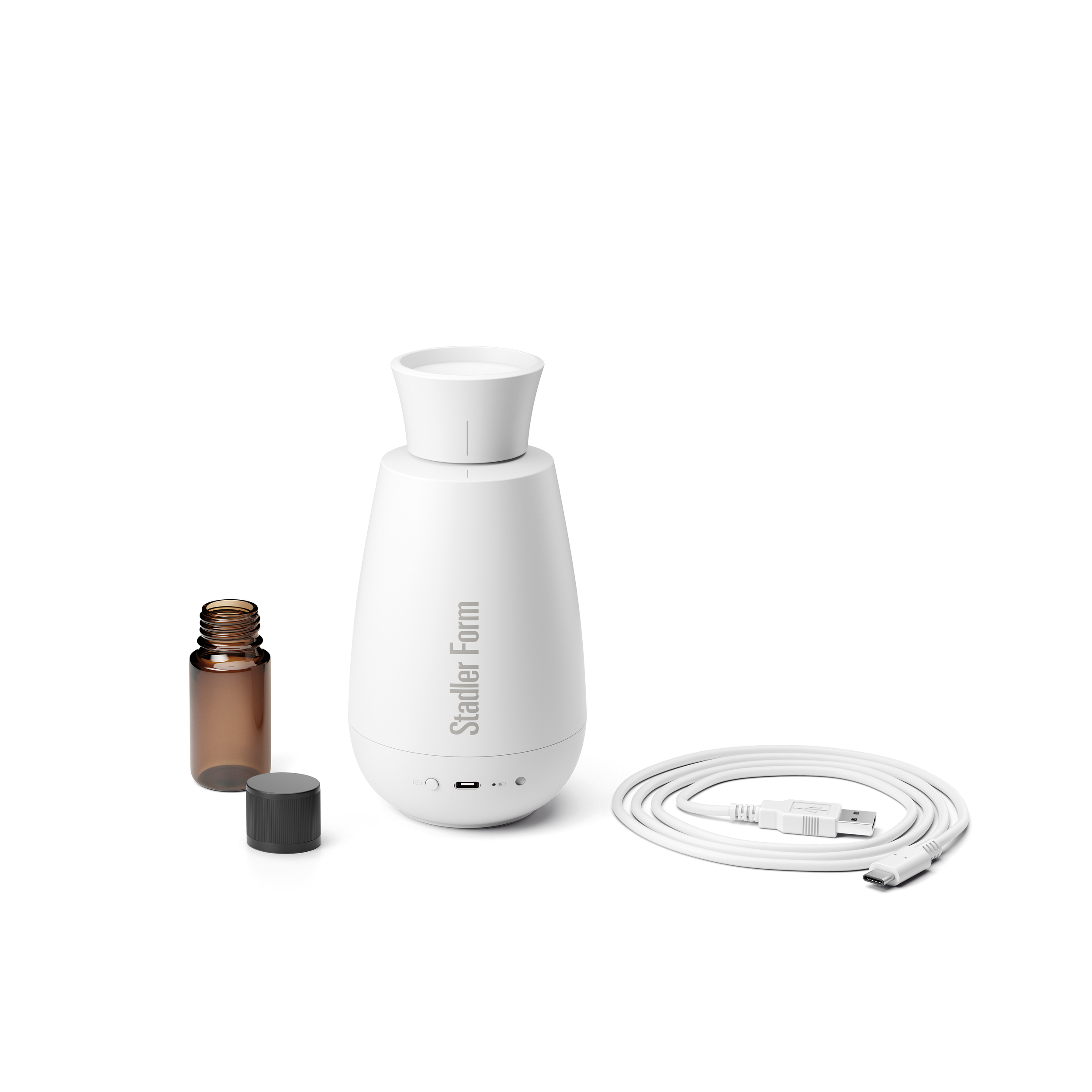 Biały dyfuzor zapachów, mała brązowa butelka olejku eterycznego i kabel USB. Wszystko na białej powierzchni.