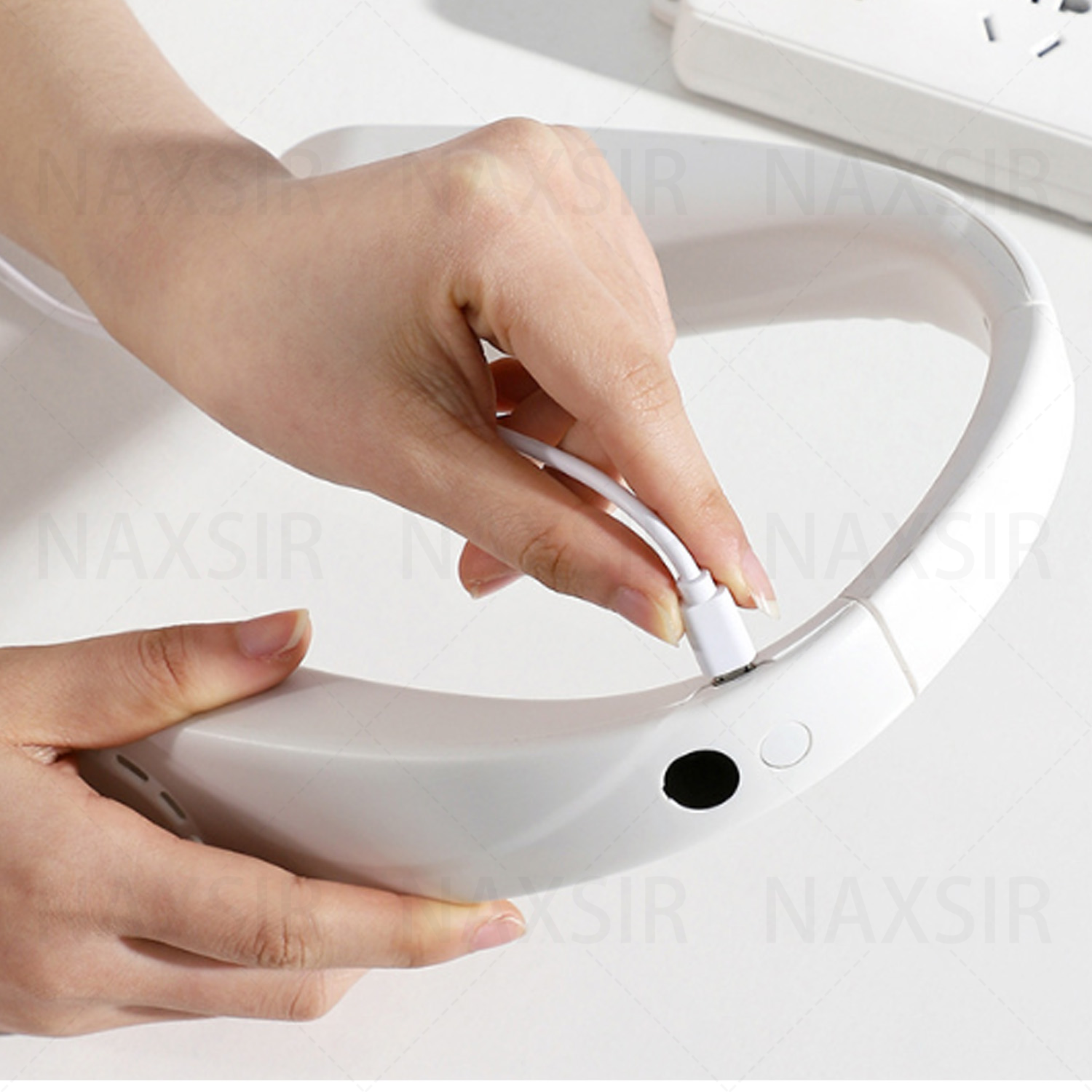 Eine Hand, die ein USB-C-Kabel in einen weißen Nackenventilator steckt. Der Ventilator steht auf einer weißen Oberfläche.