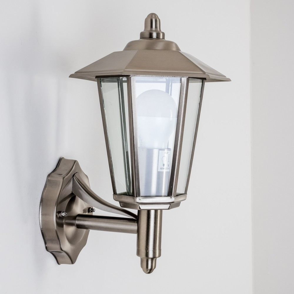 Eine silberne Wandlampe mit Glasgehäuse und weißer Glühbirne. An weißer Wand montiert.