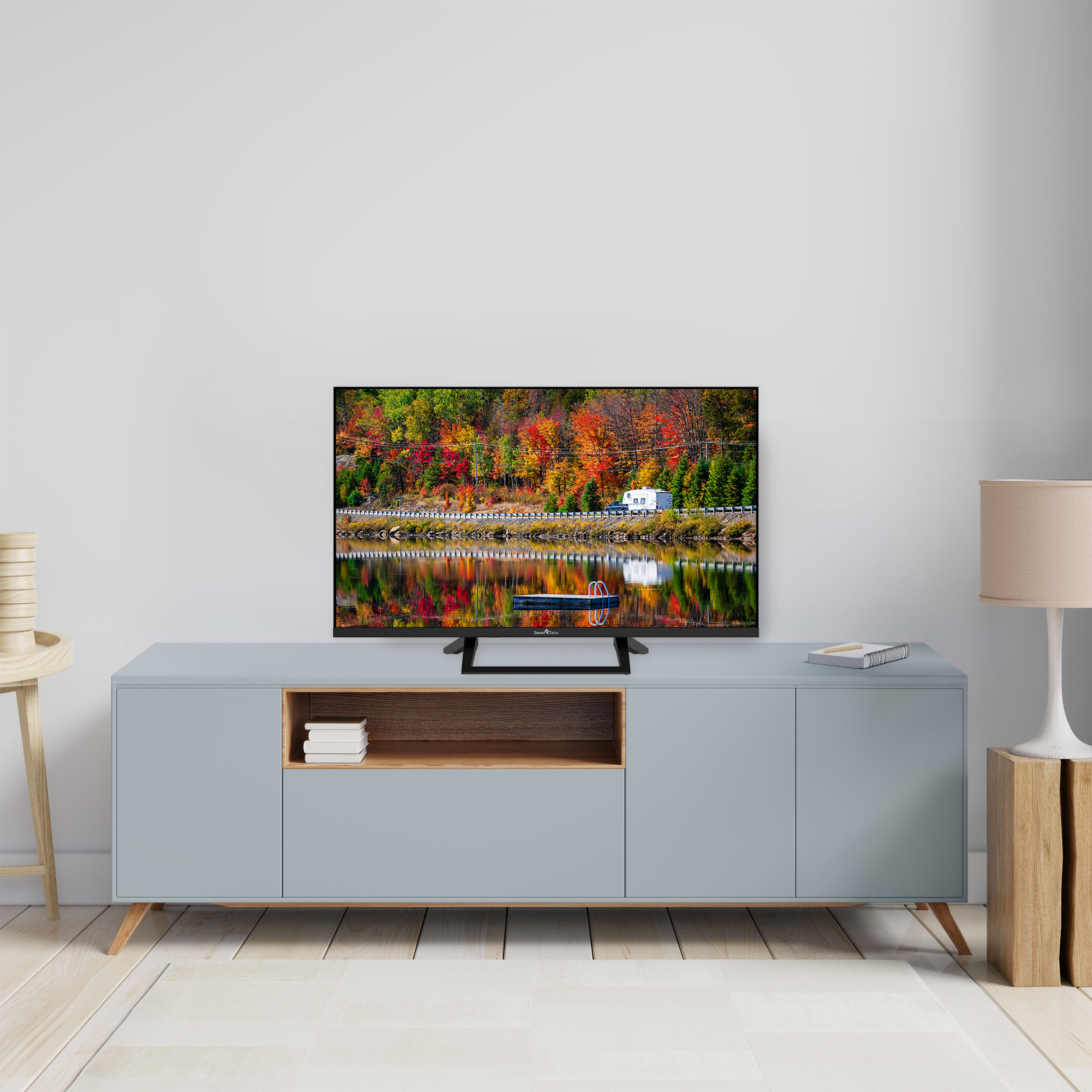 Un televisore è su un mobile azzurro, con il riflesso di una foresta colorata e acqua.