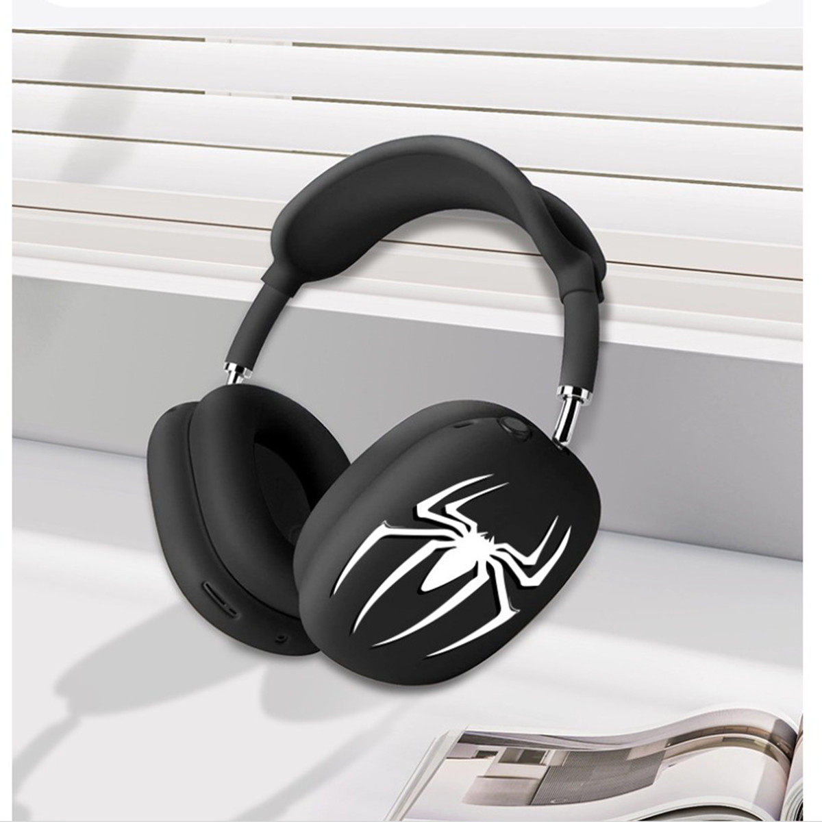 Auriculares negros con un logotipo de araña están sobre una superficie blanca. Los auriculares están cerca de una pared. El fondo es neutro.