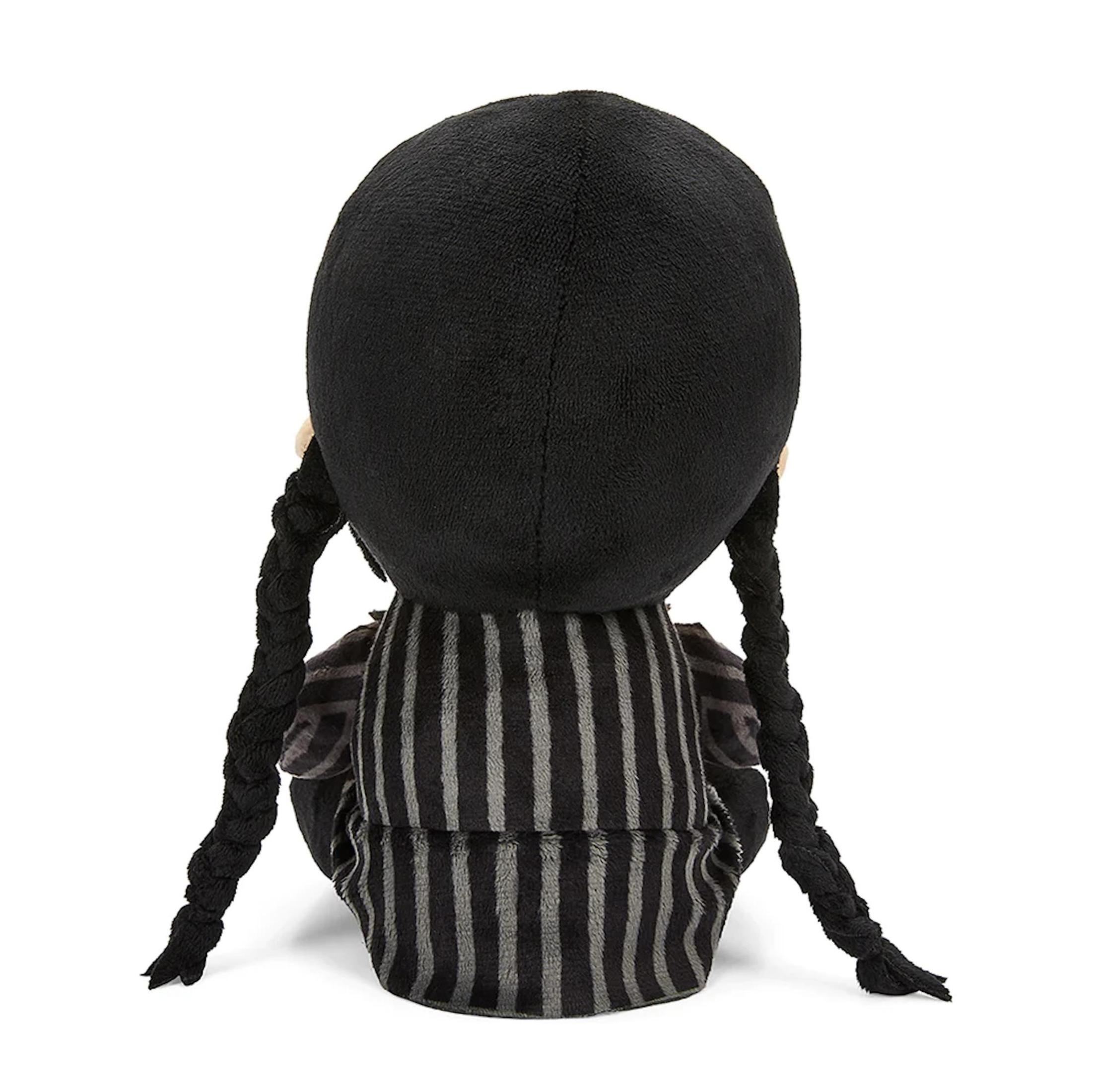 Rückansicht einer Plüschpuppe von Wednesday Addams. Sie trägt ein gestreiftes Kleid und hat schwarze Zöpfe.