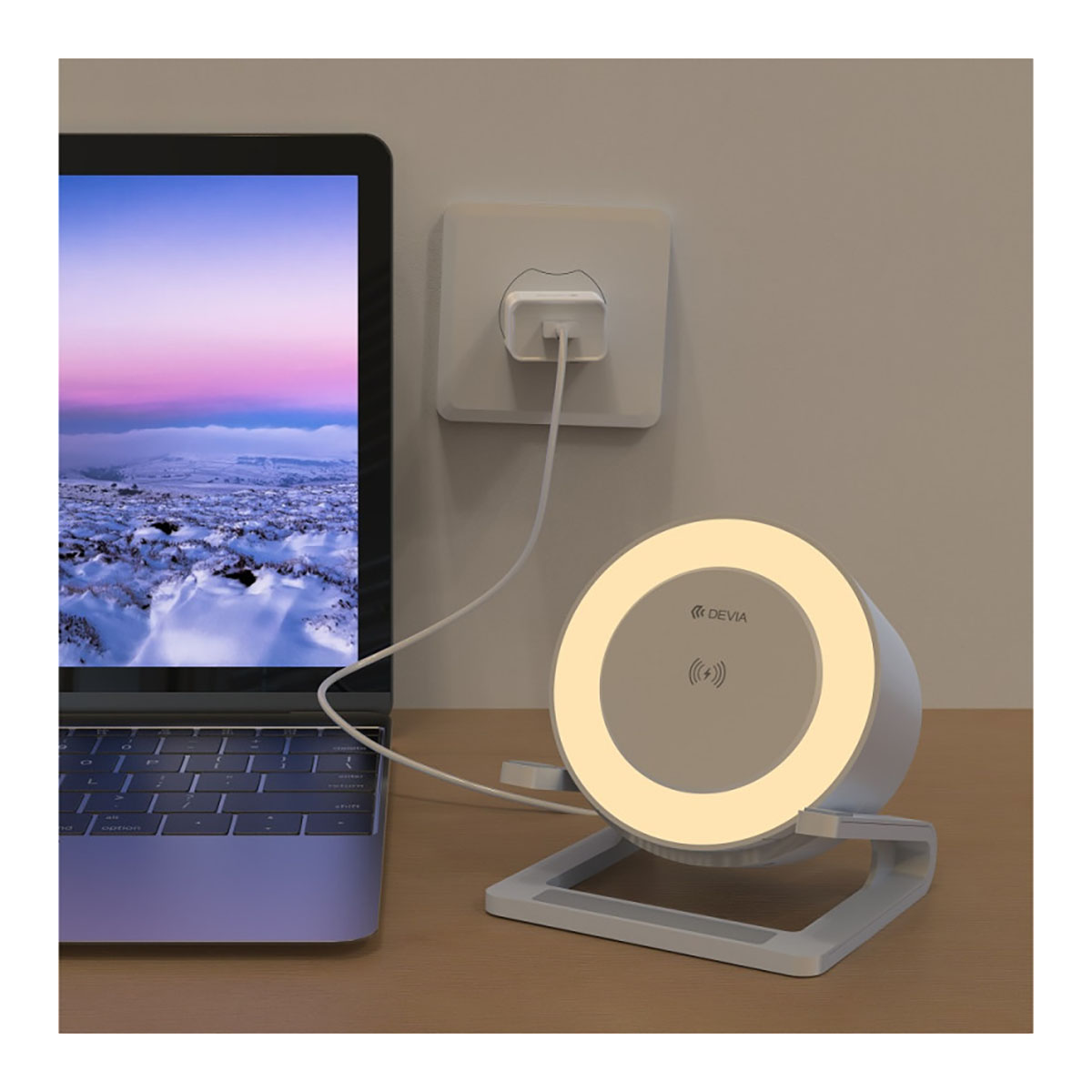 Chargeur sans fil à côté d'un ordinateur portable. Le chargeur est branché au mur. L'arrière-plan est un coucher de soleil.