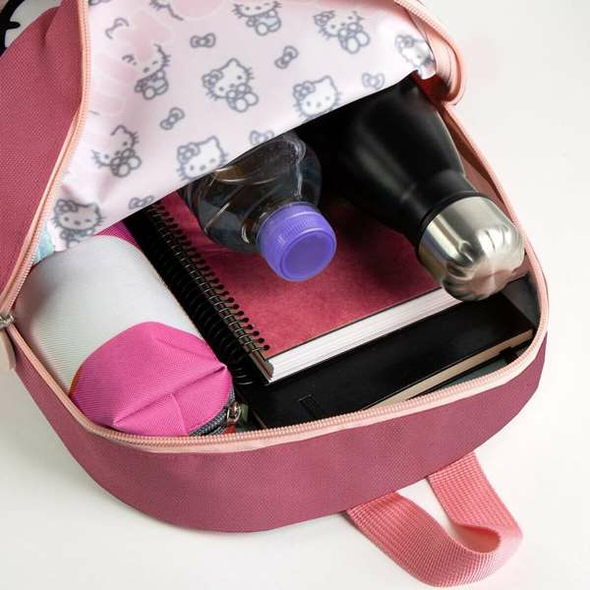 Offener Hello Kitty Rucksack, der den Inhalt zeigt: Wasserflaschen, Notizbücher und ein Federmäppchen. Rosa Innenraum.