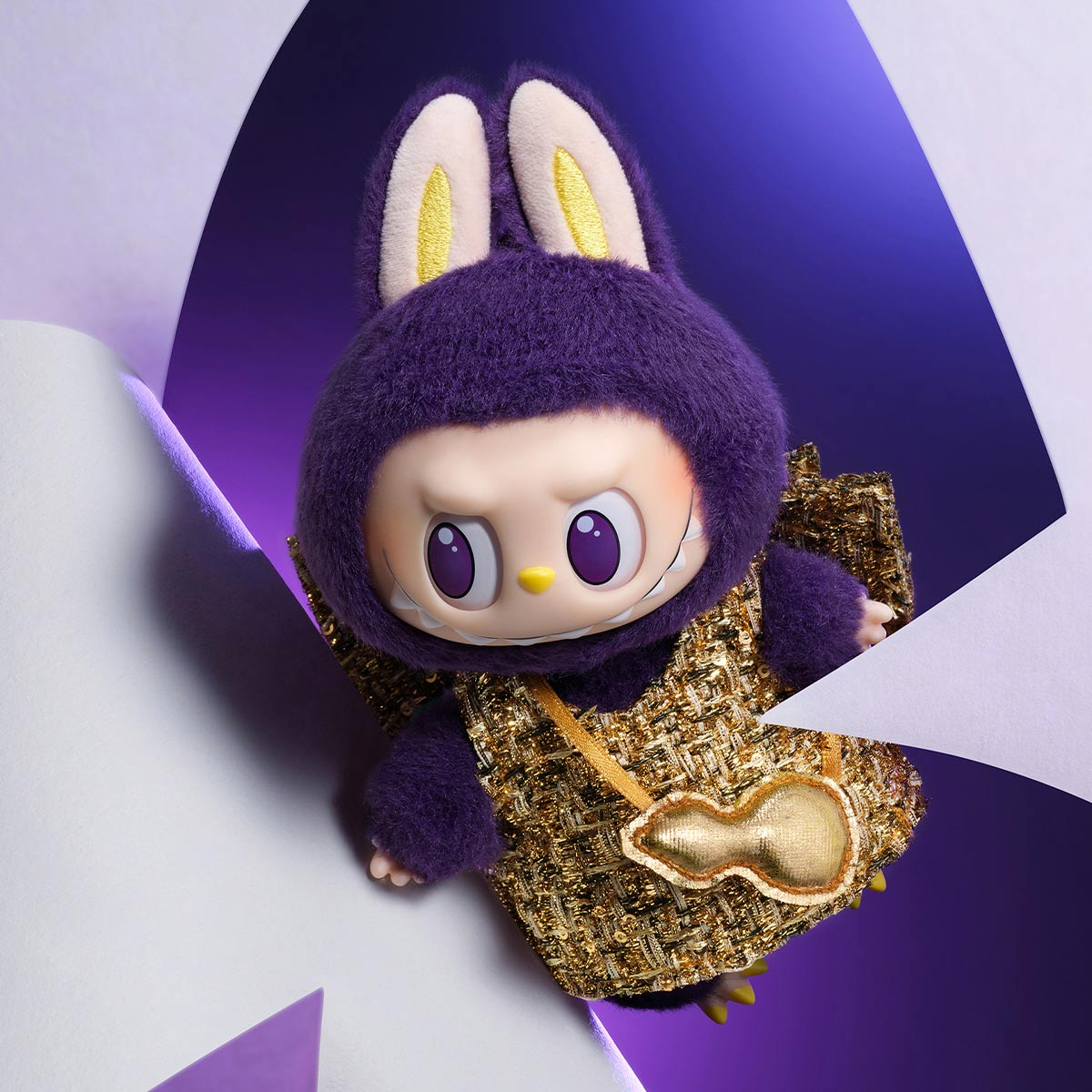 Eine Figur eines lila Hasen mit goldfarbenem Pailletten-Outfit. Sie ist zwischen weißen Papierformen positioniert.