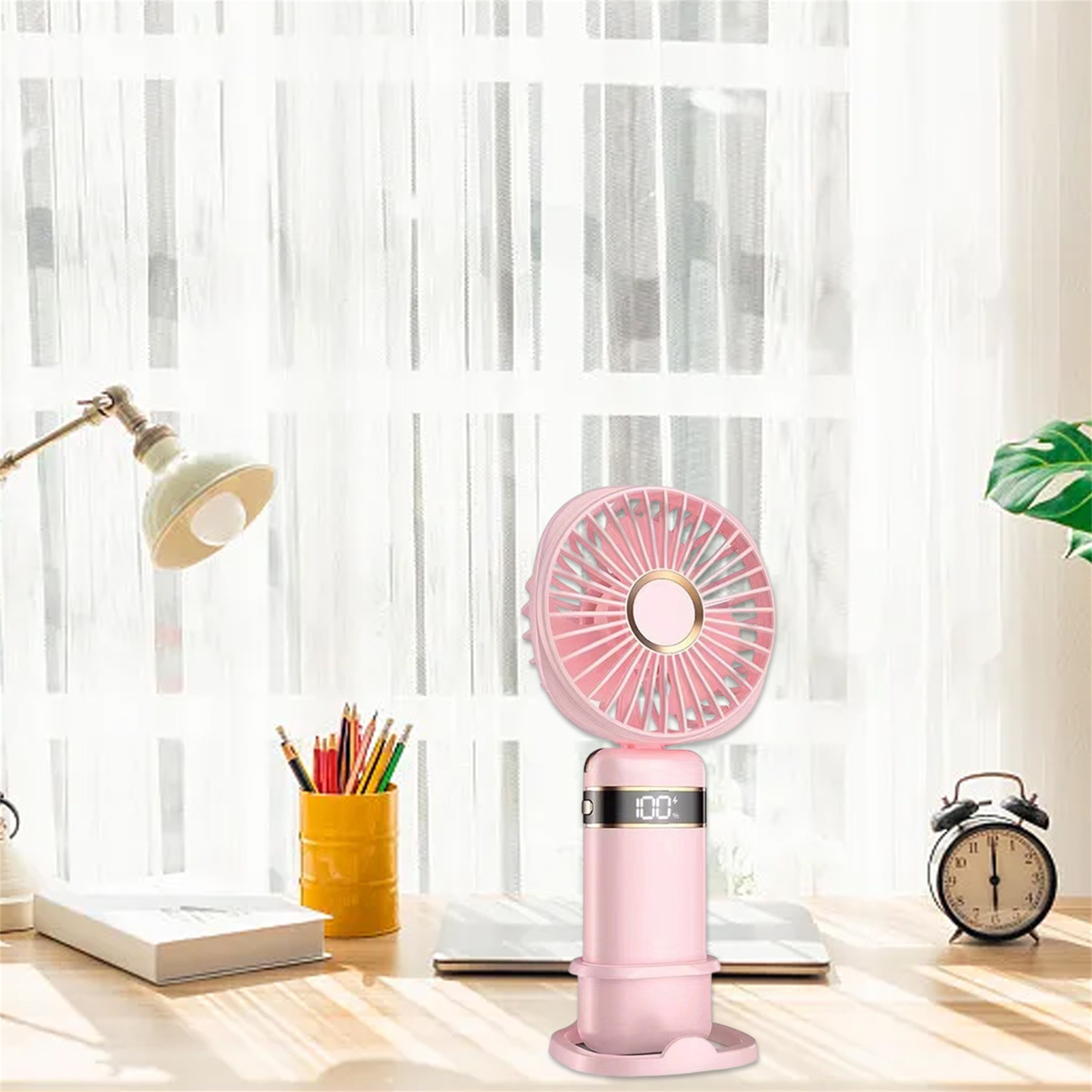 Rosa tragbarer Ventilator auf einem Schreibtisch. Lampe, Stifte und Uhr im Hintergrund.