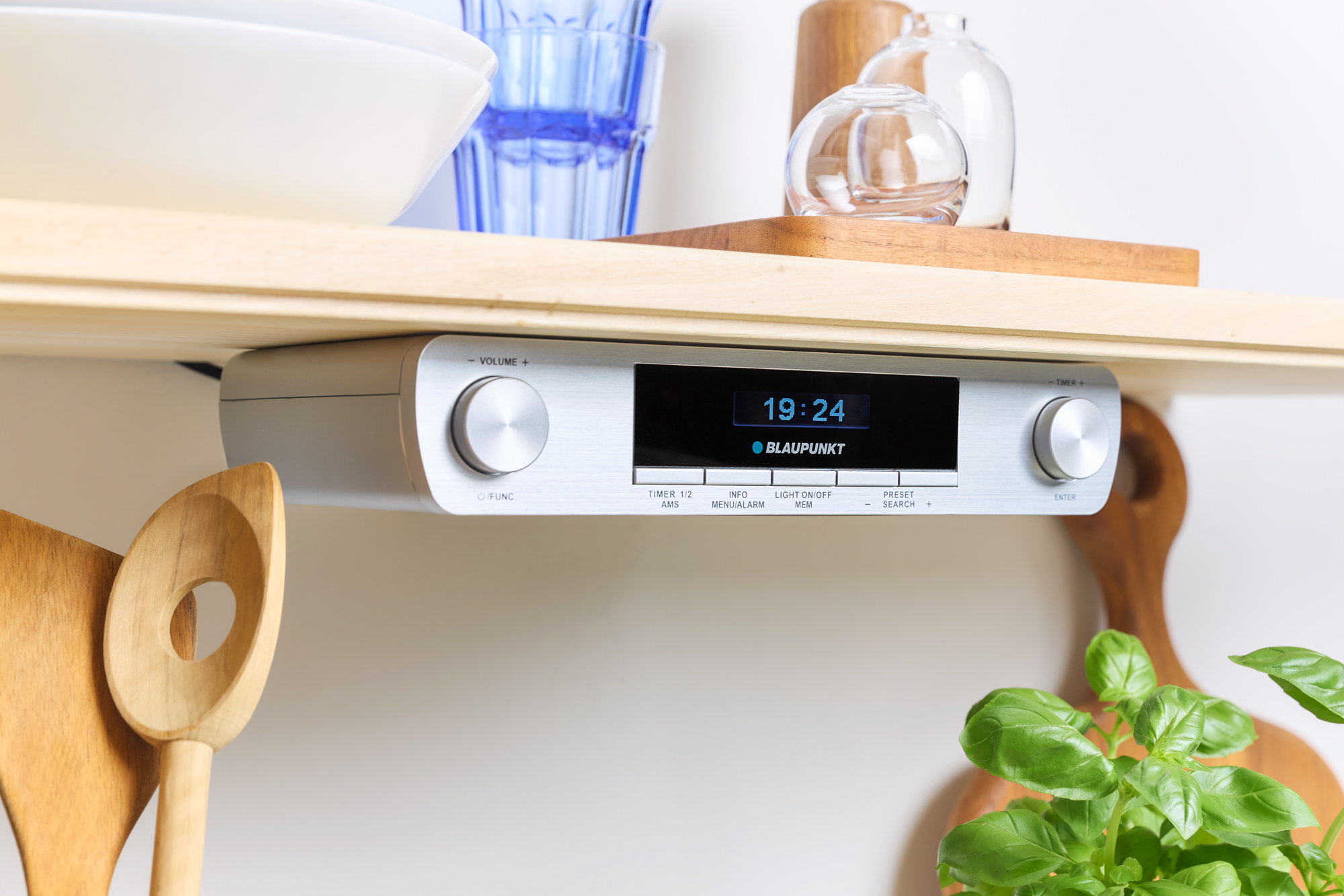 Ein silbernes Blaupunkt Audiosystem ist unter einem Regal montiert, mit angezeigter Uhrzeit (19:24) und Holzutensilien.