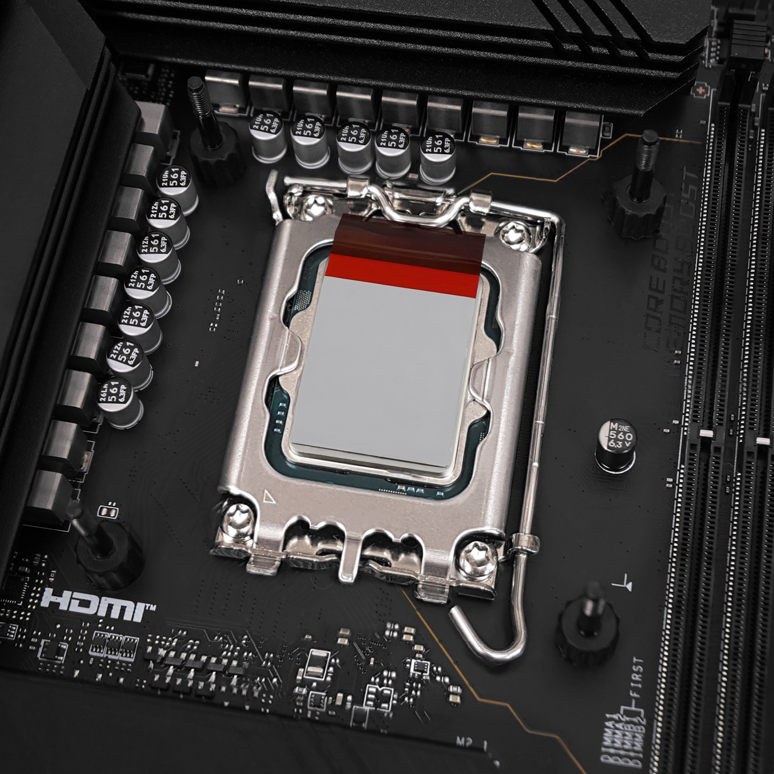 Płyta główna komputera z zainstalowaną ramką kontaktową procesora i czerwono-szarym elementem w gnieździe CPU.