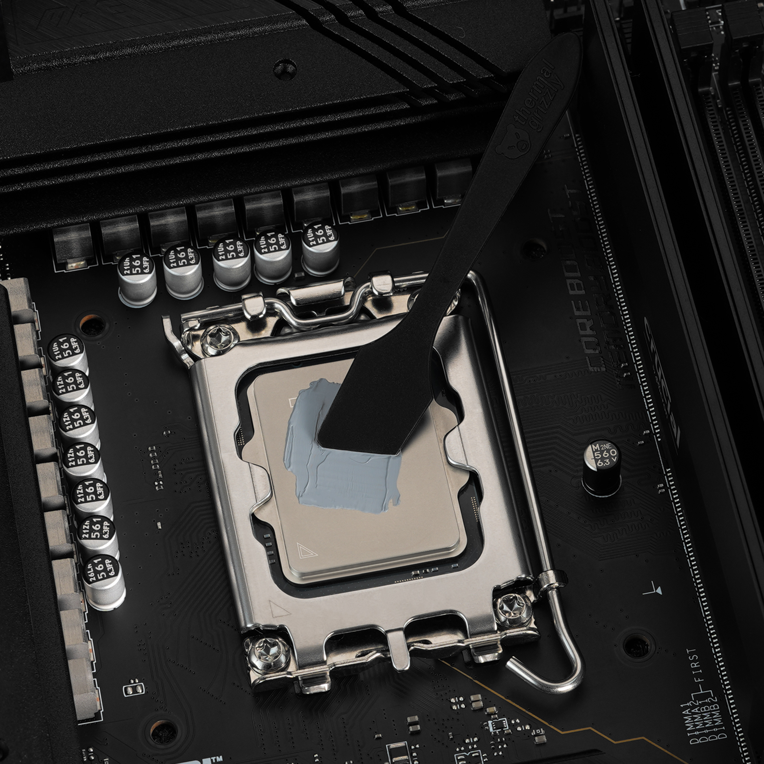 Eine CPU auf einem Motherboard, auf die mit einem Spatel Wärmeleitpaste aufgetragen wird.