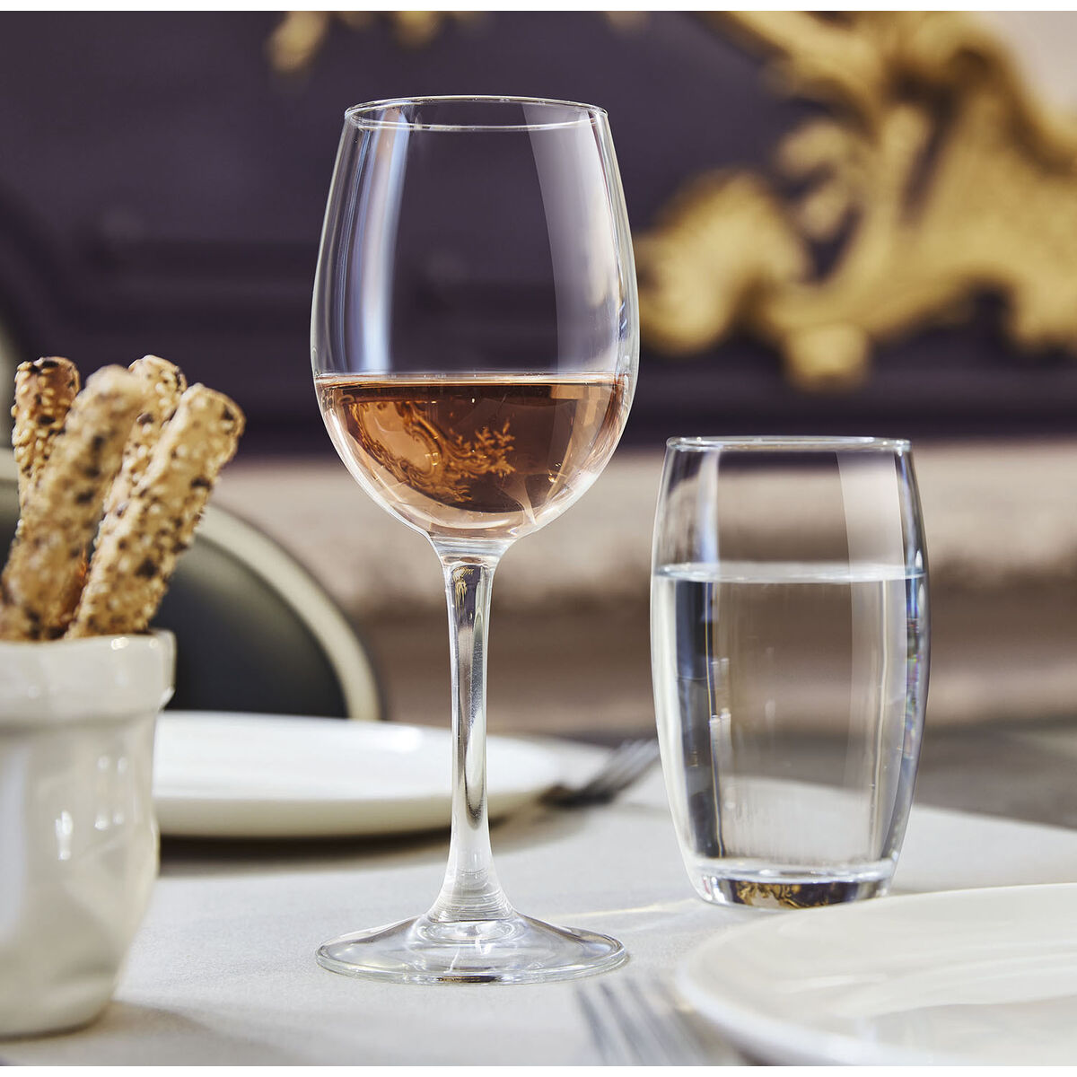 Ein Weinglas mit Roséwein, ein Wasserglas und Brotstangen auf einem Tisch.