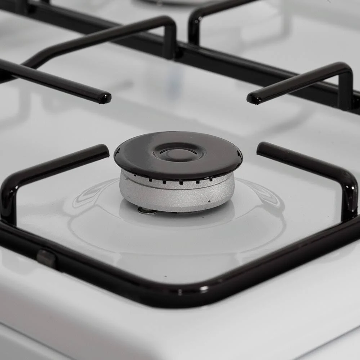 Primer plano de un quemador de cocina de gas. El quemador es negro, con superficie blanca. Hay rejillas negras.