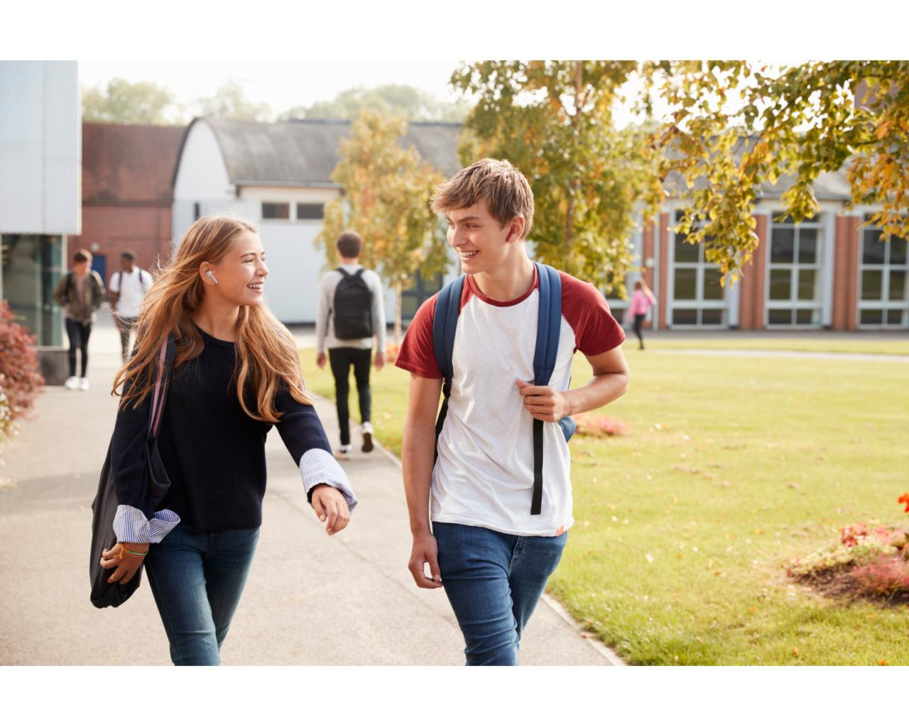 Dwóch uśmiechniętych uczniów idących ścieżką. W tle budynki i drzewa.