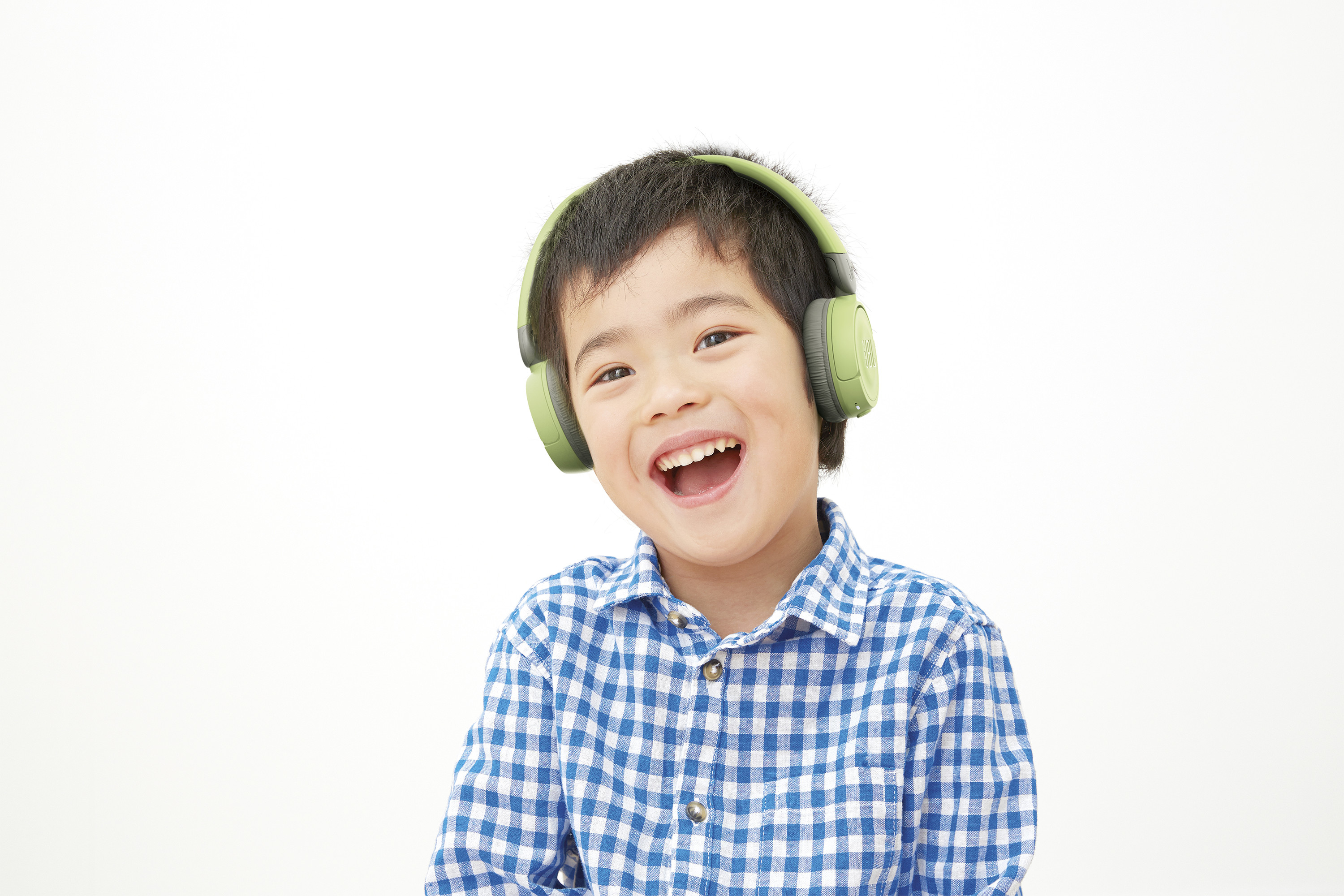 Un niño pequeño con auriculares verdes, sonriendo y riendo. Lleva una camisa a cuadros azul.
