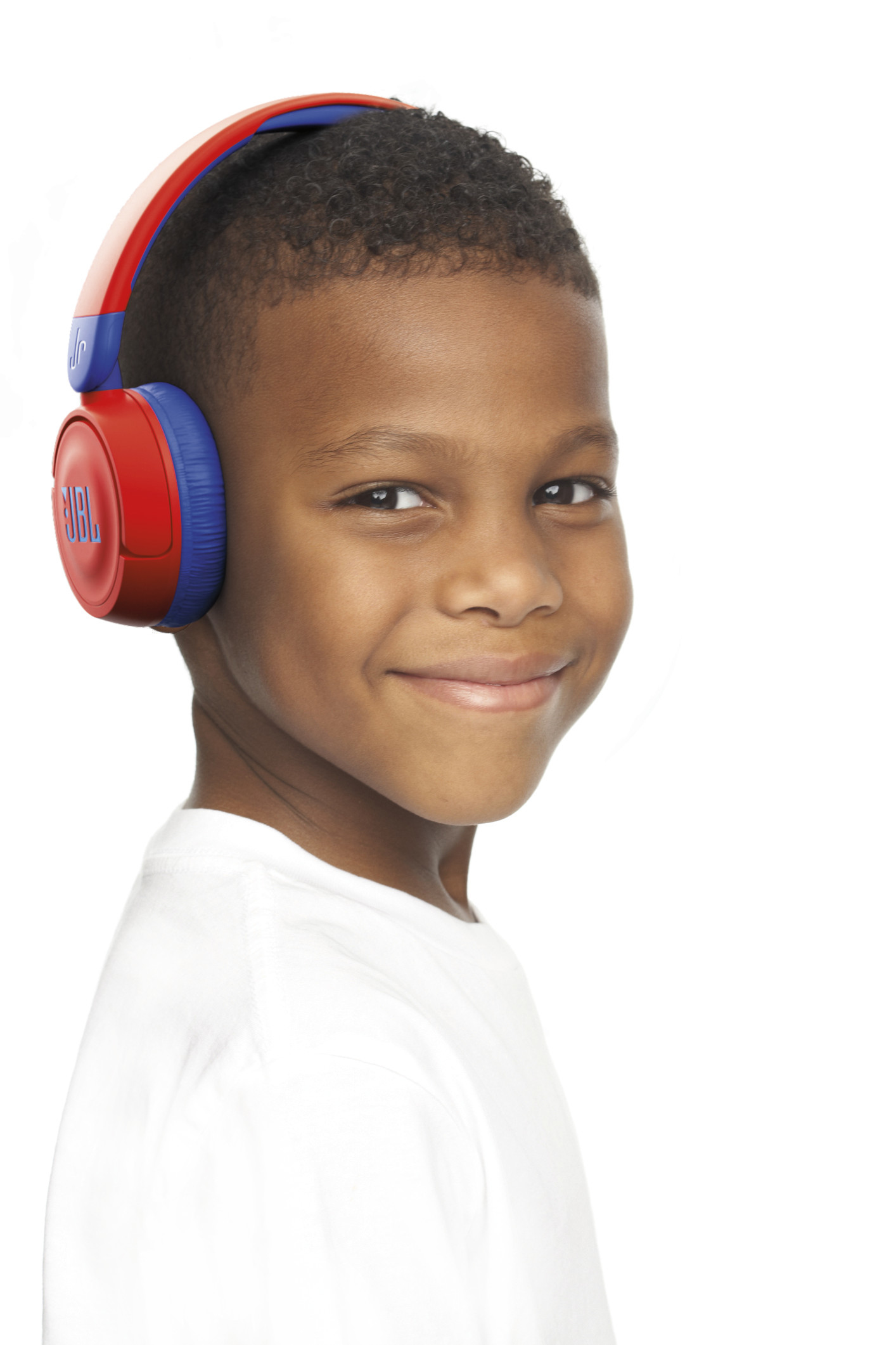 Un niño pequeño con auriculares JBL rojos y azules sonríe a la cámara.