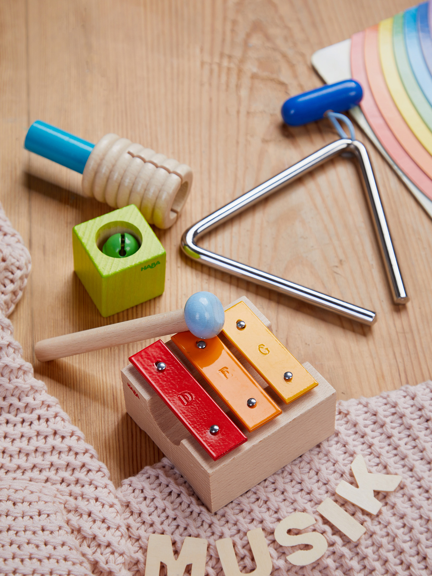 Musikinstrumente auf Holz: Xylophon, Dreieck, Rassel und ein Holzblock mit grüner Glocke.