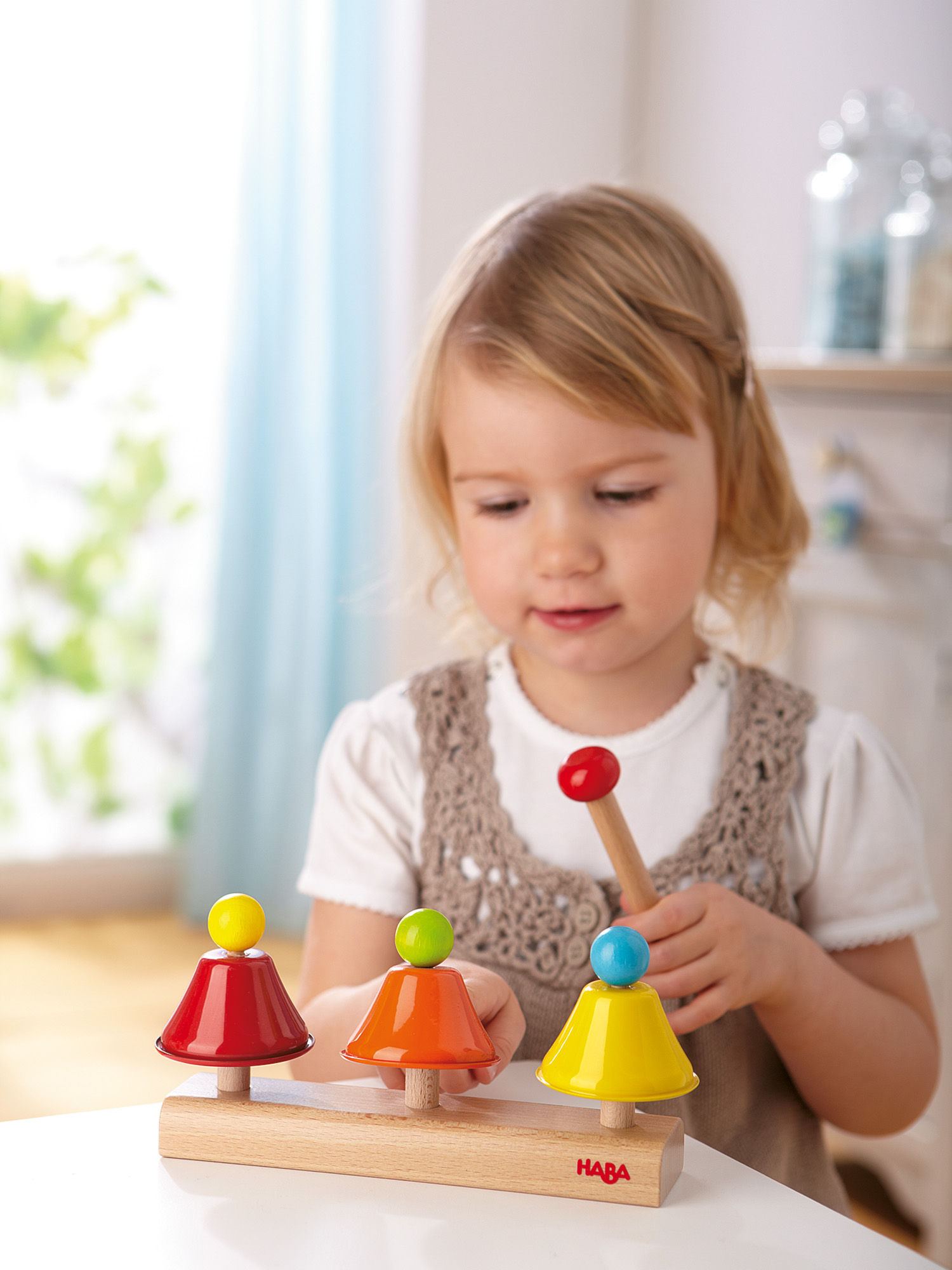 Ein junges Mädchen spielt mit einem Holzspielzeug. Das Spielzeug hat Glocken und einen Hammer. Der Hintergrund ist unscharf.
