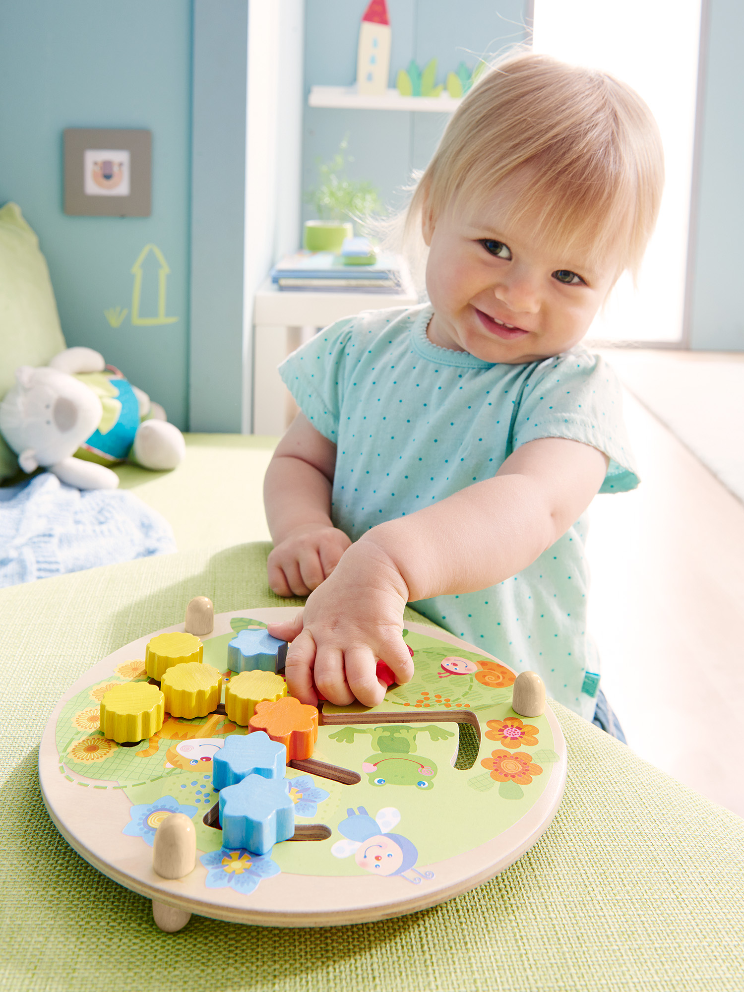 Ein Kleinkind spielt mit einem Holzspielzeug. Das Spielzeug hat bunte Formen und einen Hammer. Das Kind lächelt.