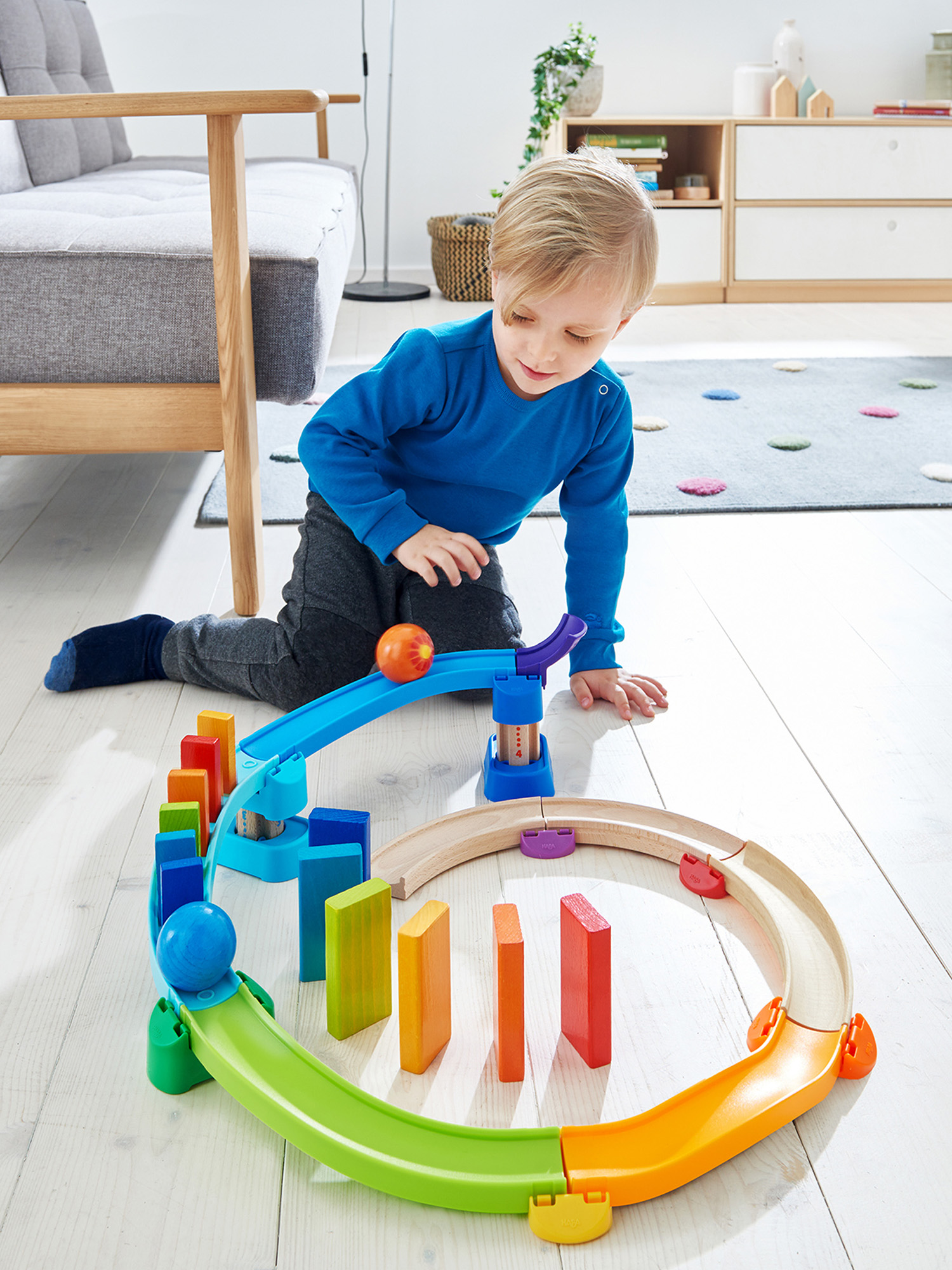 Ein Kind spielt mit einem Spielzeug-Zug-Set. Das Set enthält eine Strecke, Dominosteine und eine blaue Rampe.