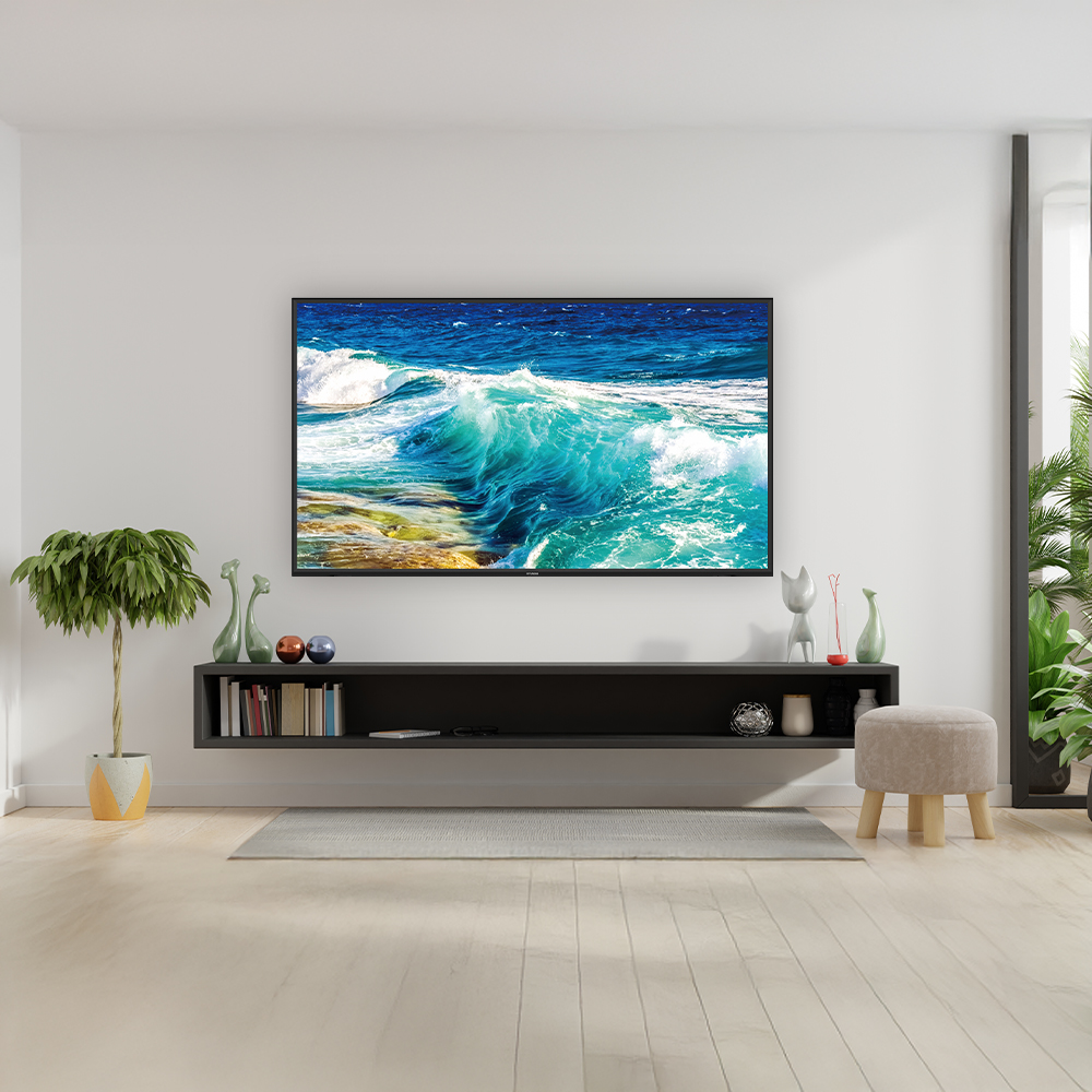 Una sala de estar con un televisor grande que muestra una escena de océano turquesa. Una estantería negra, plantas y un taburete abajo.