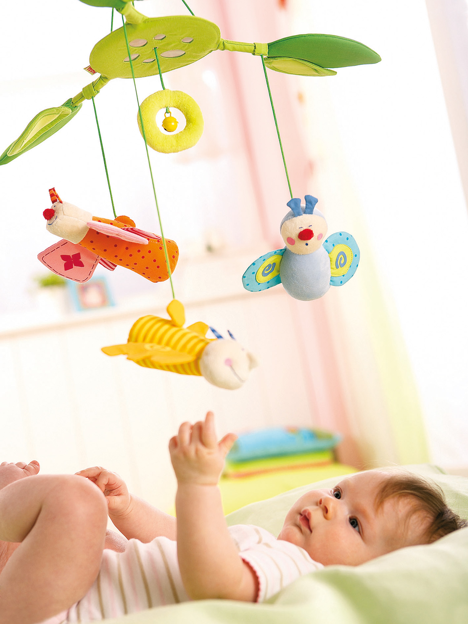 Ein Baby liegt auf einer grünen Oberfläche und greift nach einer Spieluhr mit bunten Spielzeugen.