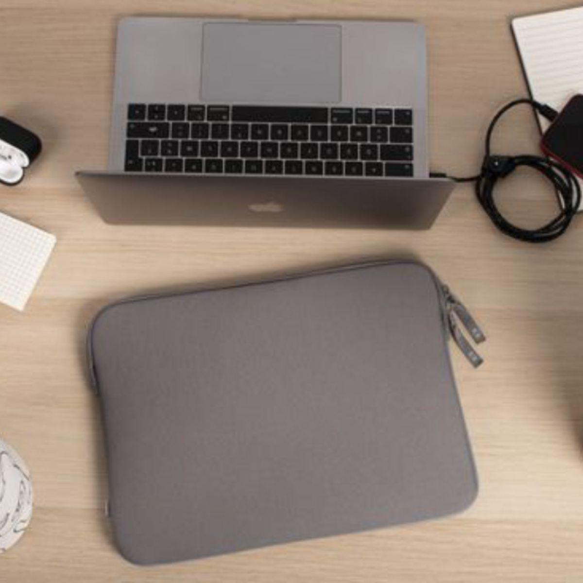 Una custodia per laptop grigia su un tavolo di legno, con un laptop, delle cuffie e un telefono.