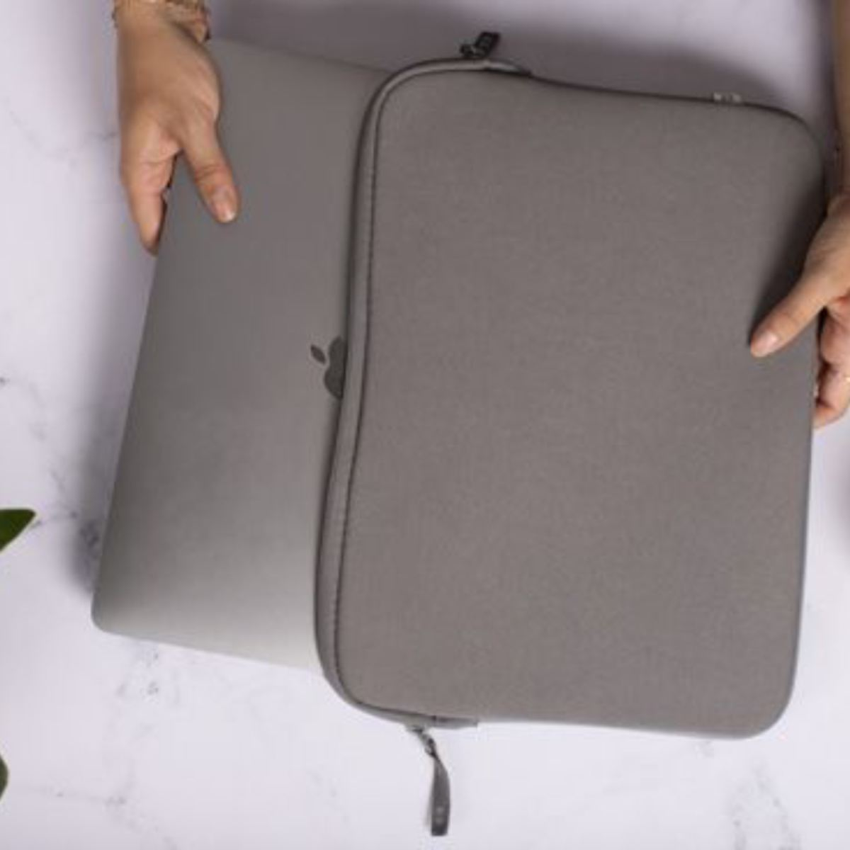 Mani che tengono un laptop grigio all'interno di una custodia grigia. Il logo Apple è visibile.