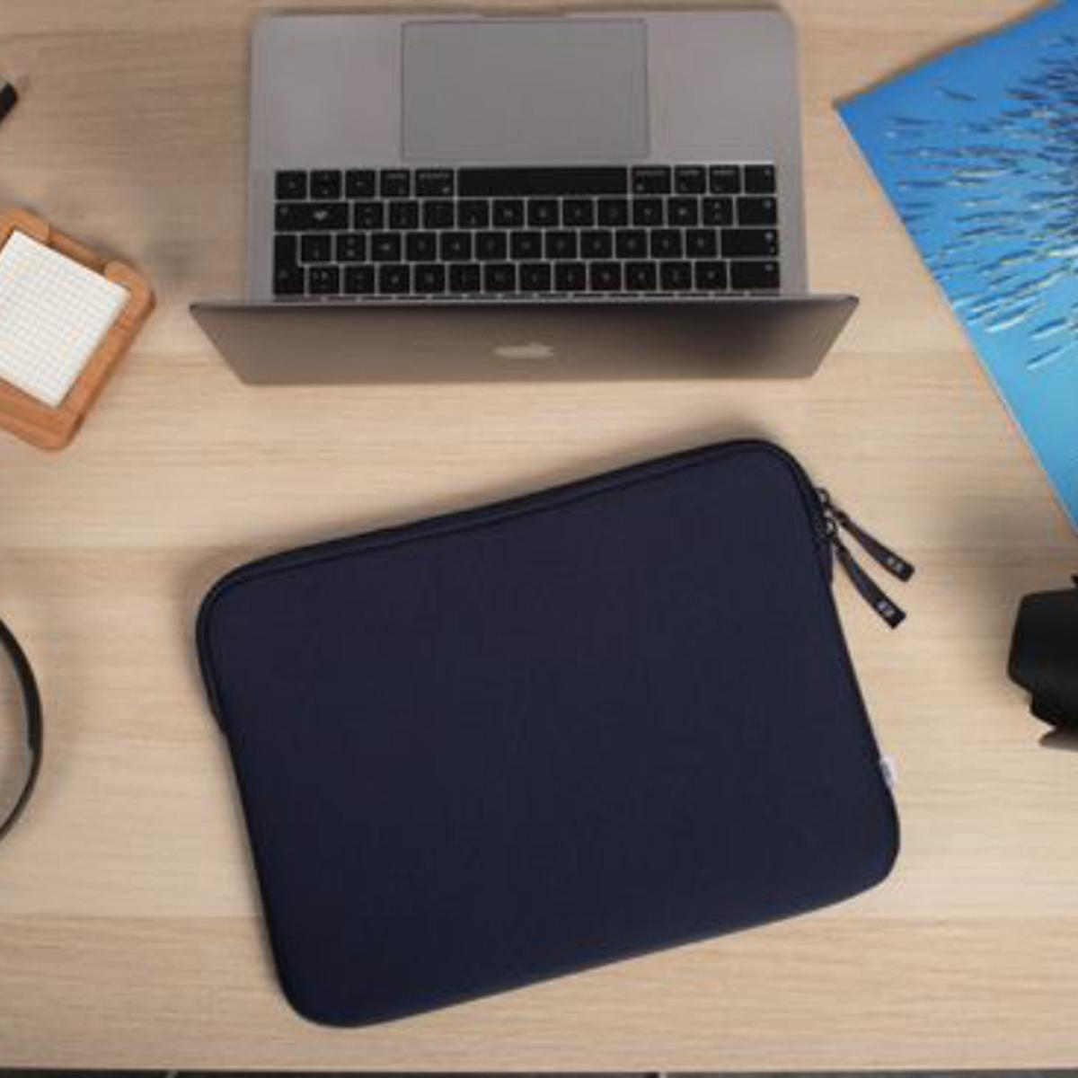 Marineblaue Laptoptasche mit Laptop. Die Tasche liegt auf einem Holztisch neben anderen Gegenständen.
