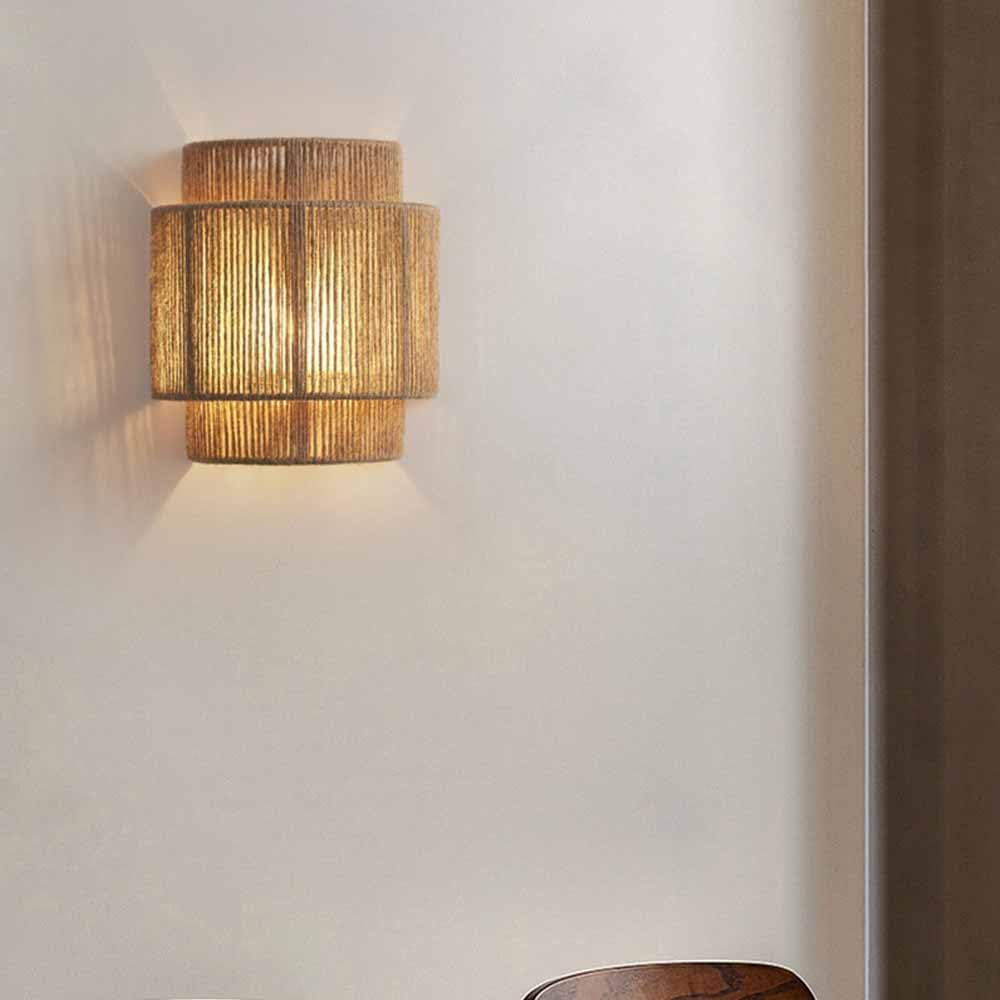 Lámpara de pared con pantalla texturizada de material tejido, emite una luz cálida.