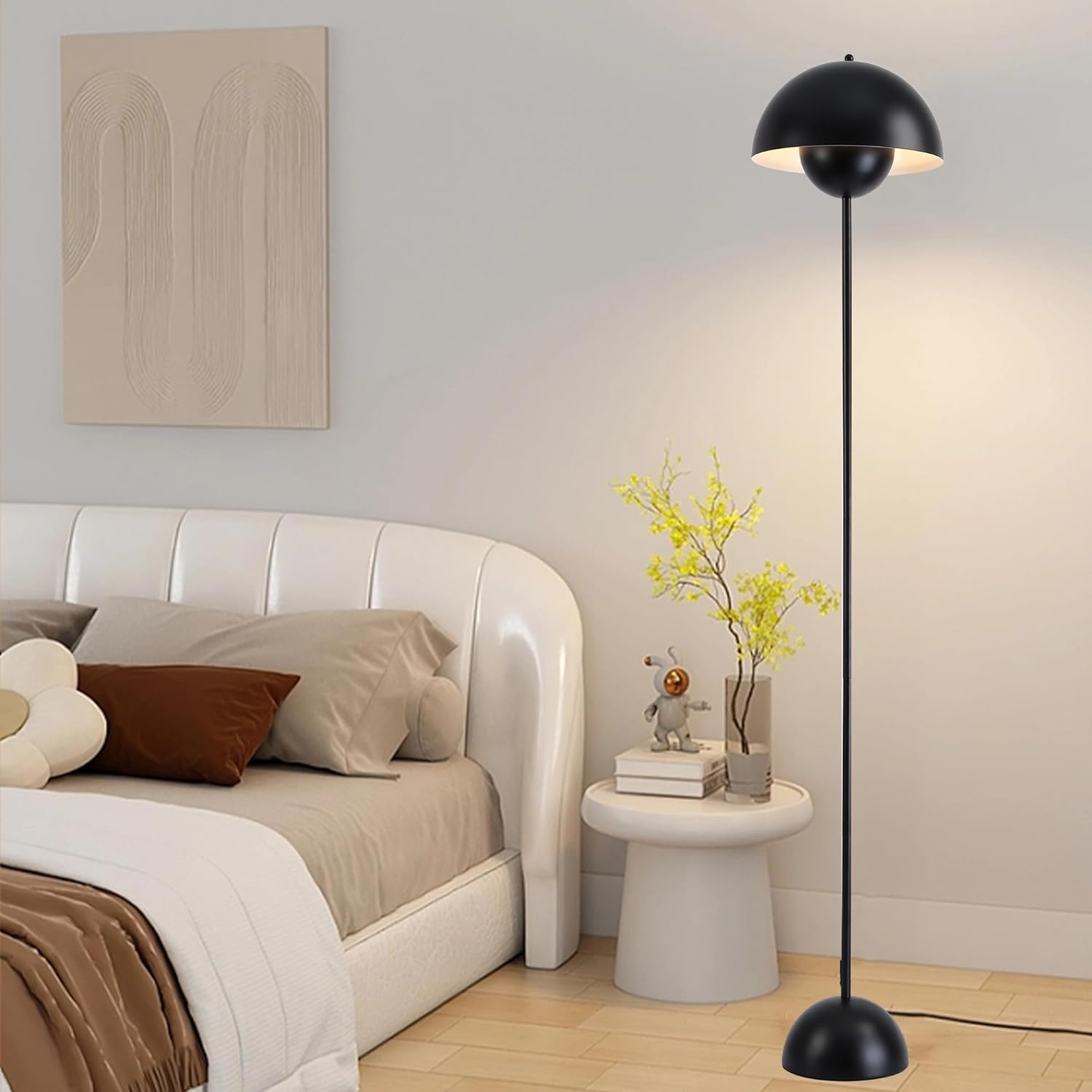 Lámpara de pie negra con pantalla redonda en una habitación. Cama, mesita con planta detrás.
