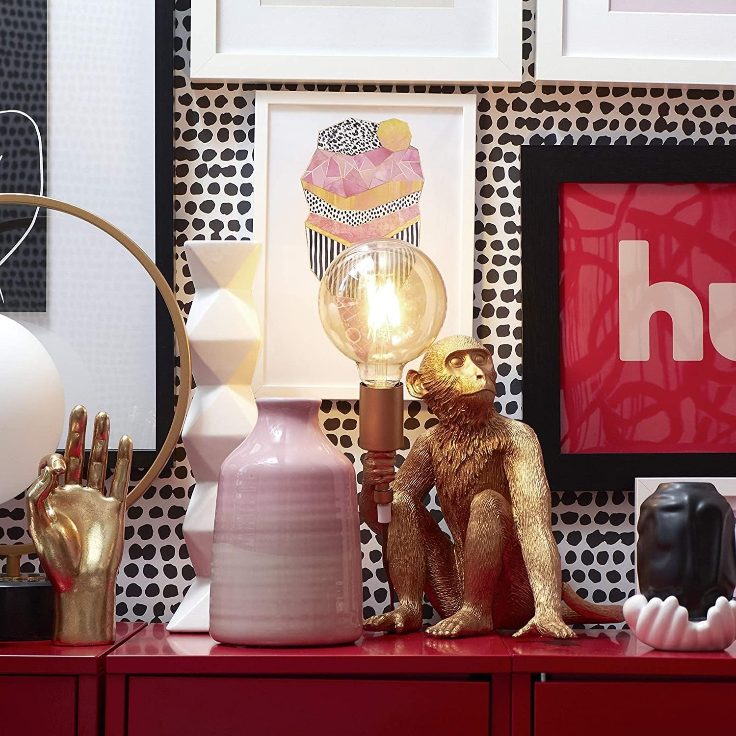 Una habitación con varias obras de arte, lámparas y objetos decorativos en una estantería roja.