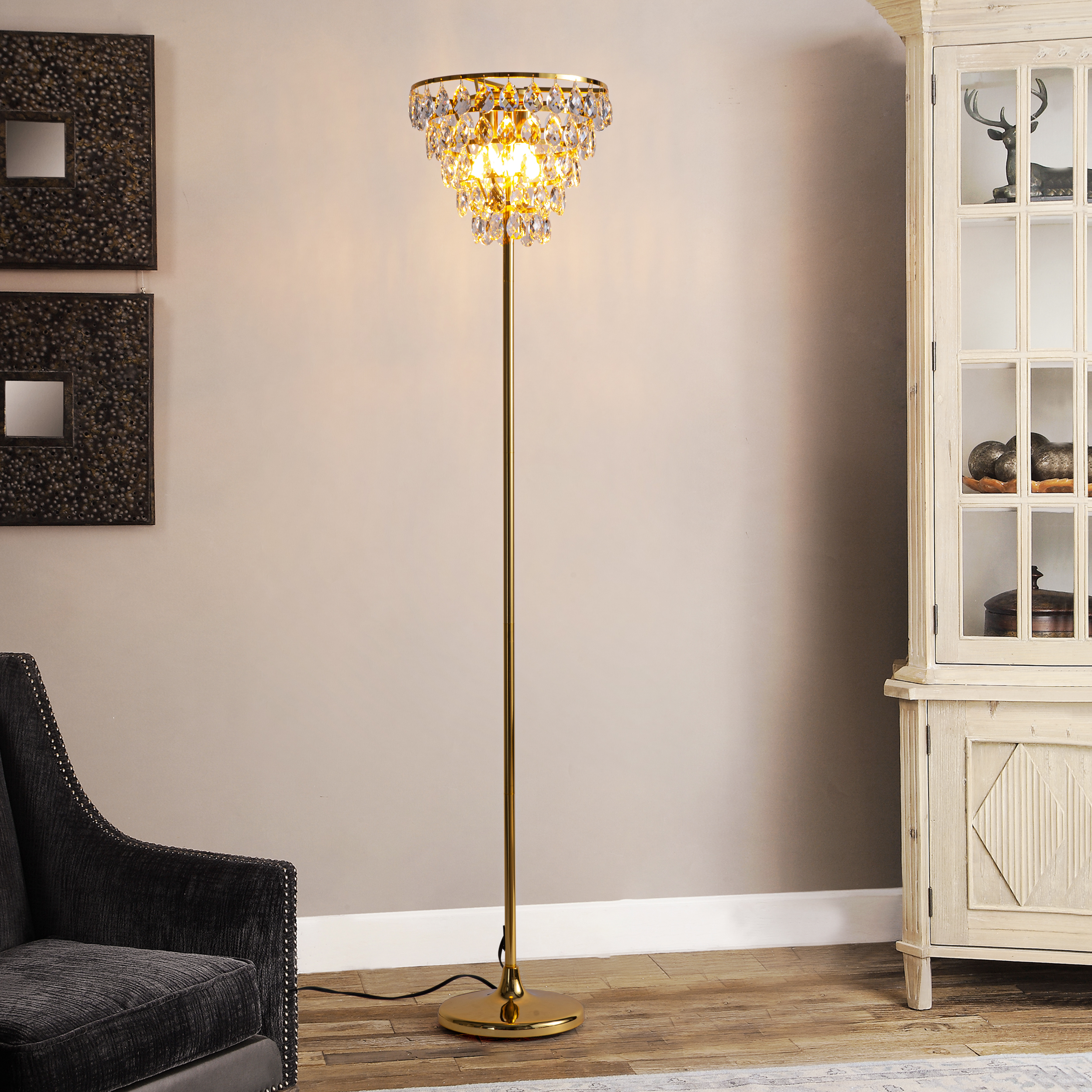 Una lámpara de pie dorada con una parte superior estilo candelabro de cristal, en una habitación con una silla negra y un mueble.