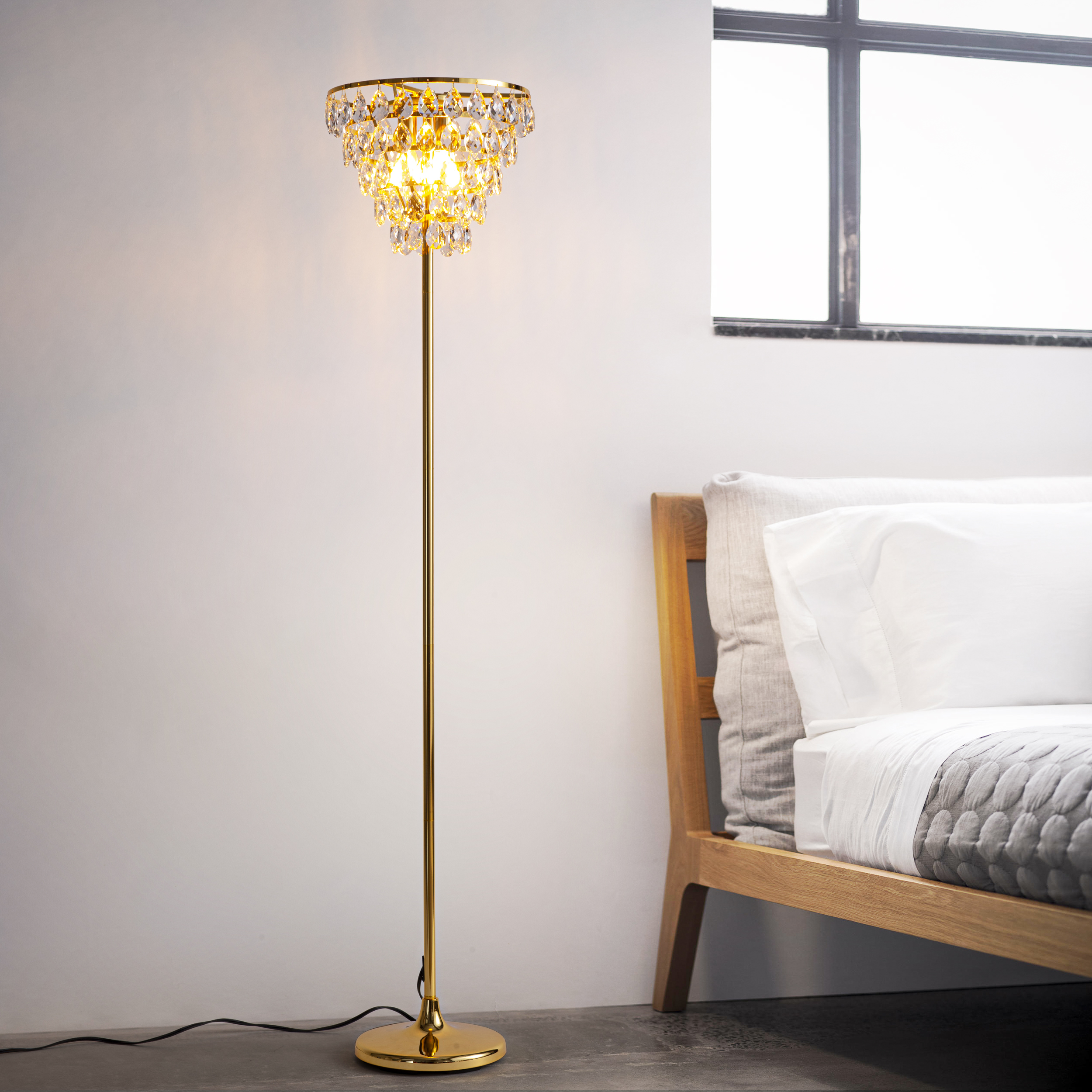 Una lámpara de pie dorada con una parte superior estilo candelabro de cristal, en un dormitorio con una cama.