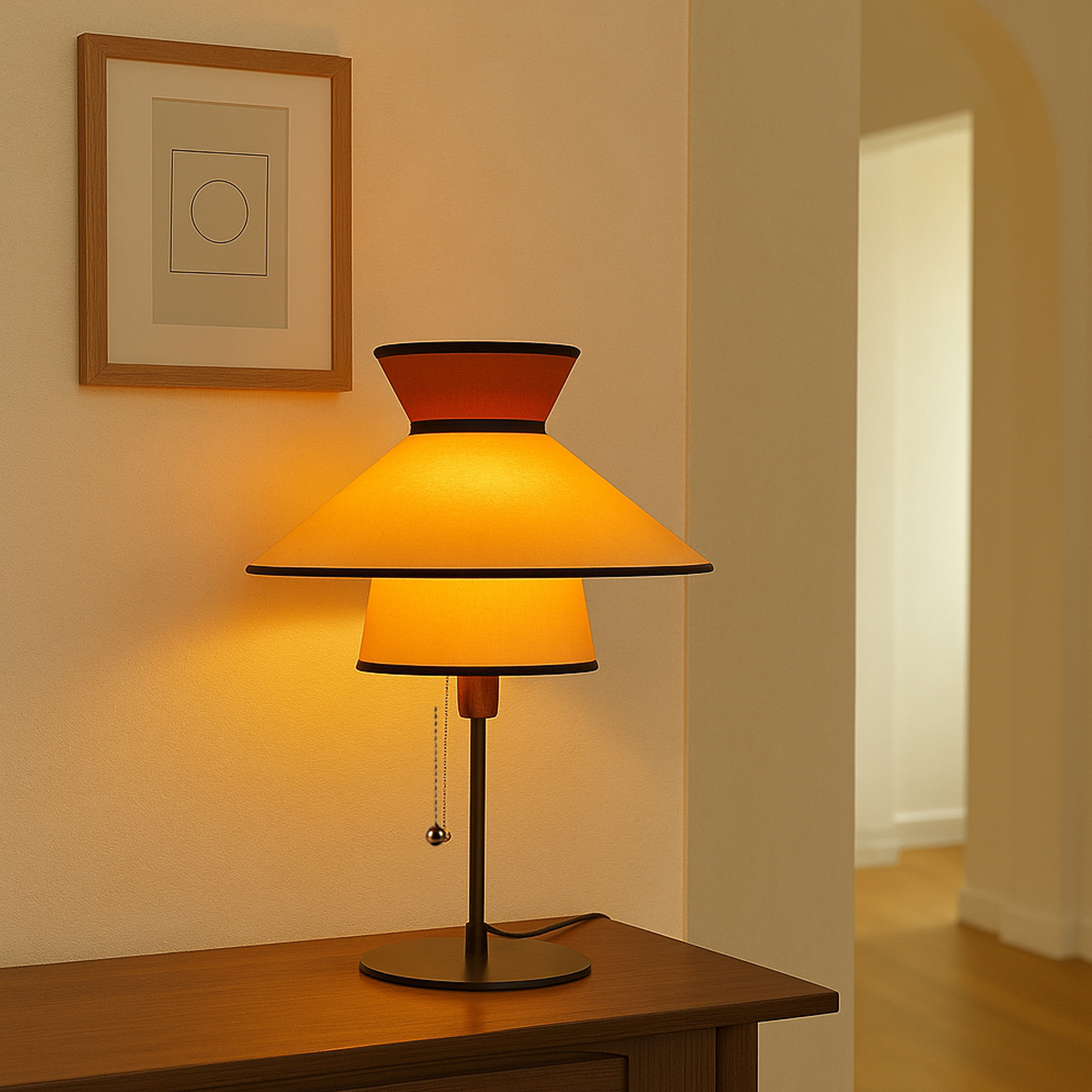 Una lámpara de mesa con dos pantallas, la inferior naranja. Está sobre un mueble de madera.