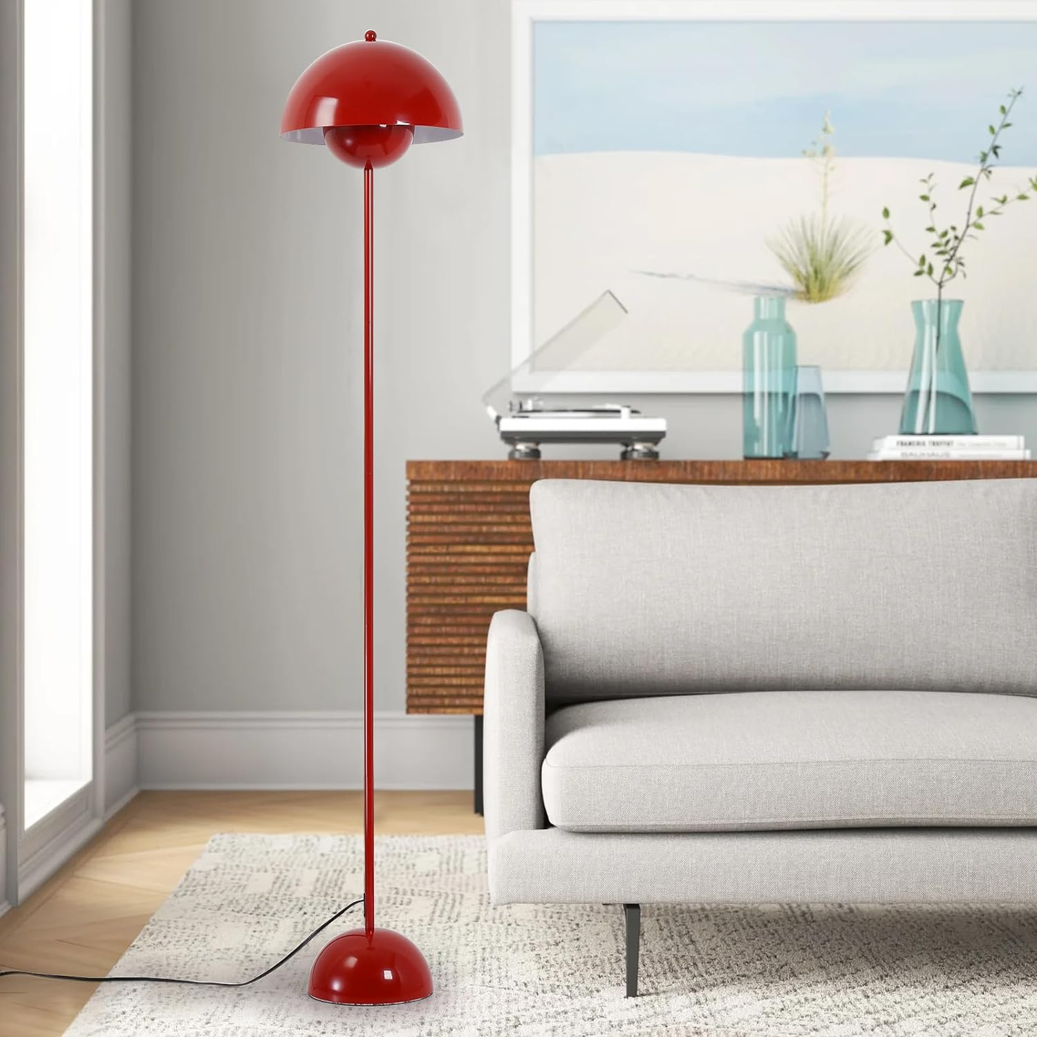 Lámpara de pie roja con pantalla redonda, cerca de un sofá y una pintura de escena playera.