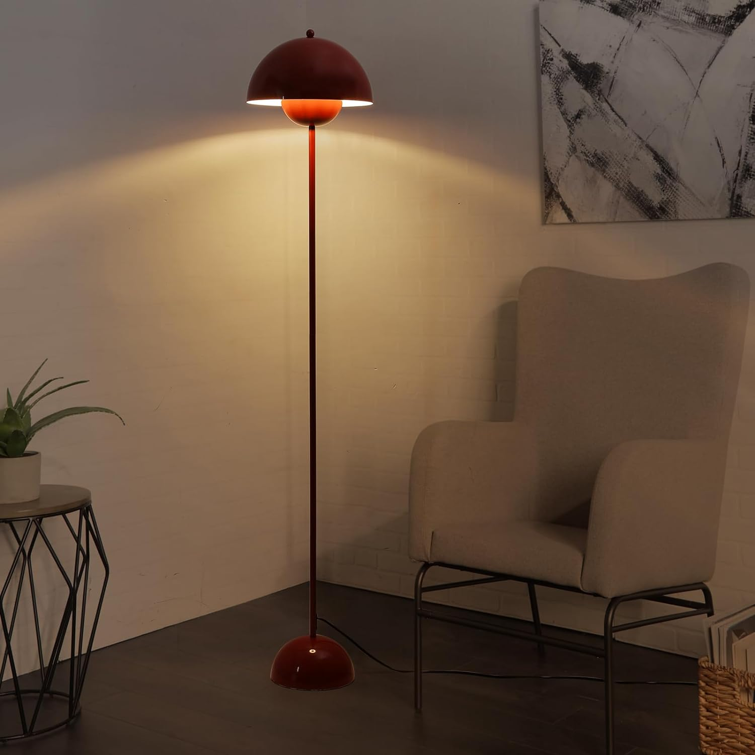 Lámpara de pie roja con pantalla redondeada, iluminando una habitación. Se ven un sillón y mesa auxiliar.