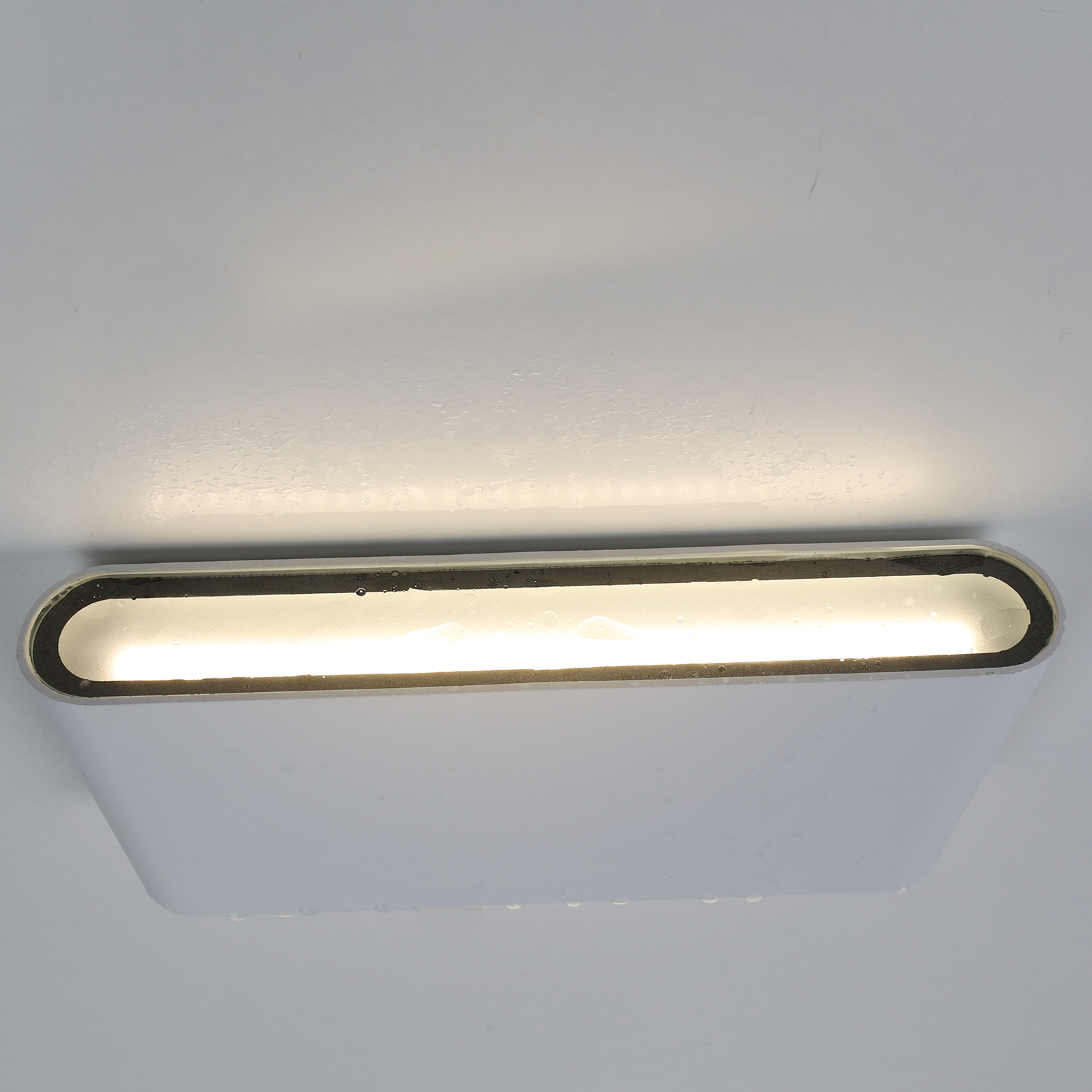 Una luz de pared blanca contra una pared blanca. La luz está encendida y emitiendo luz.