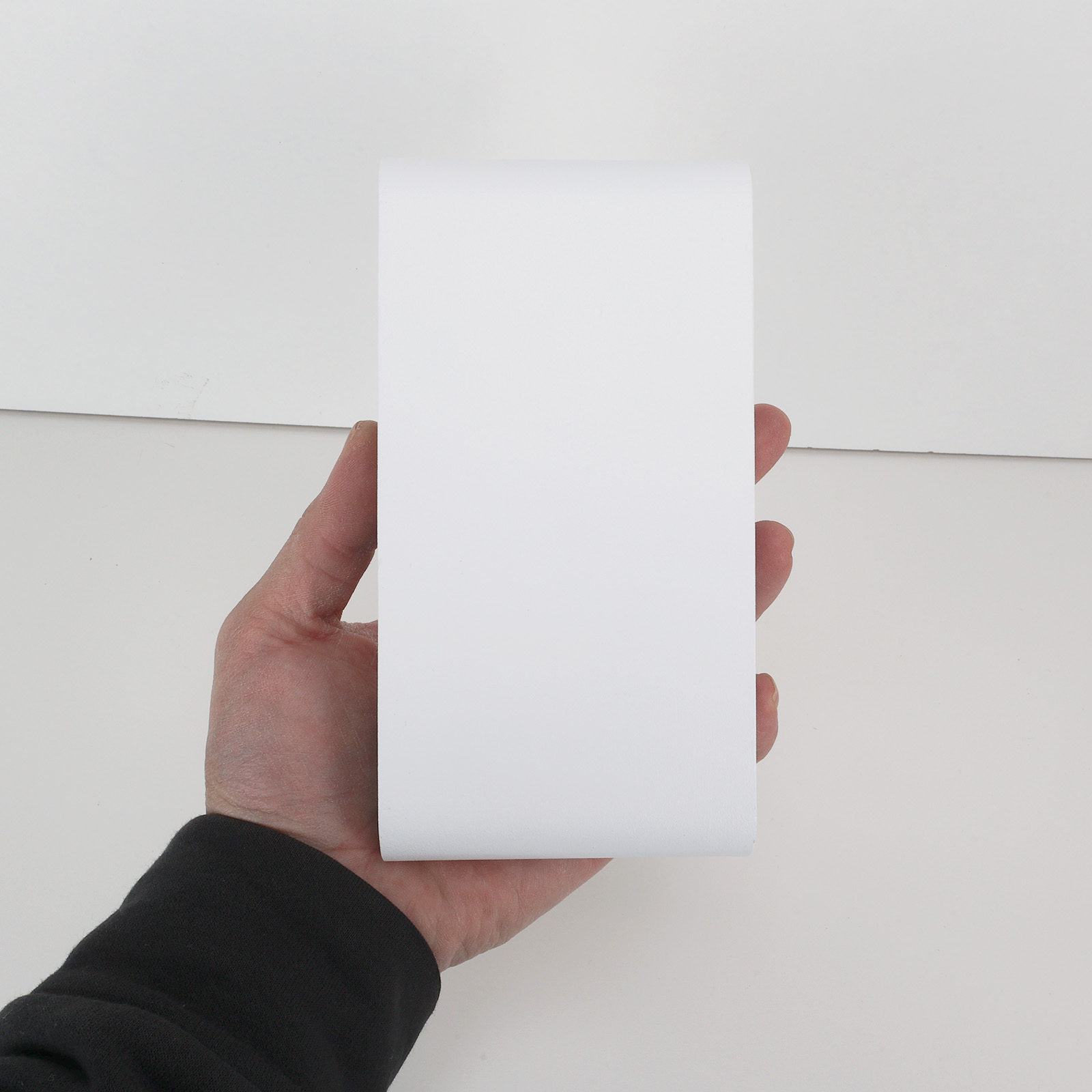Una mano sosteniendo un objeto rectangular blanco. El objeto es liso y curvo en la parte superior e inferior.
