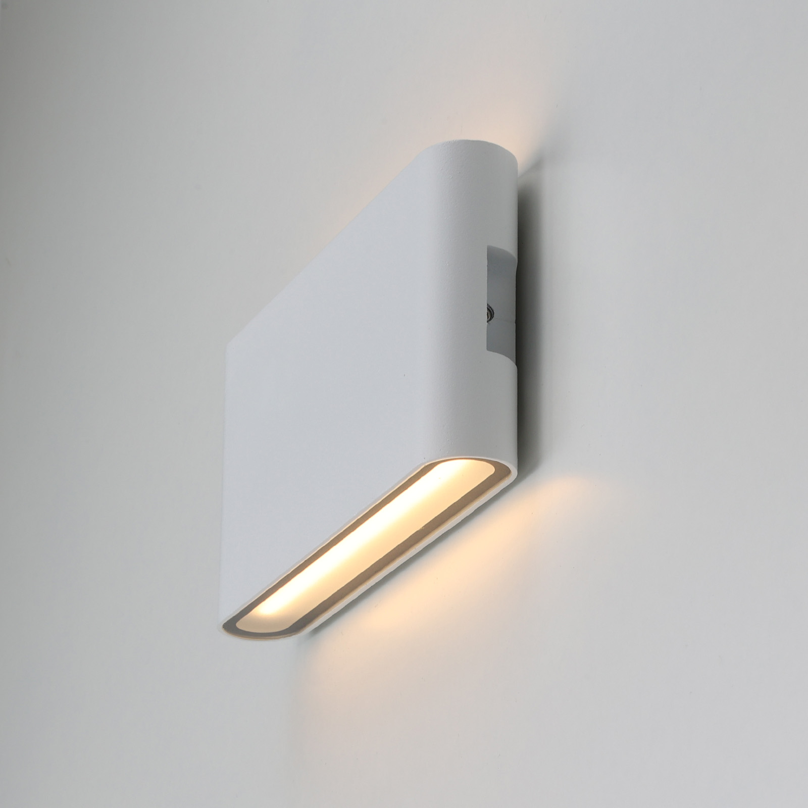 Una luz de pared blanca moderna con un diseño curvo, que emite luz suave sobre una pared neutra.