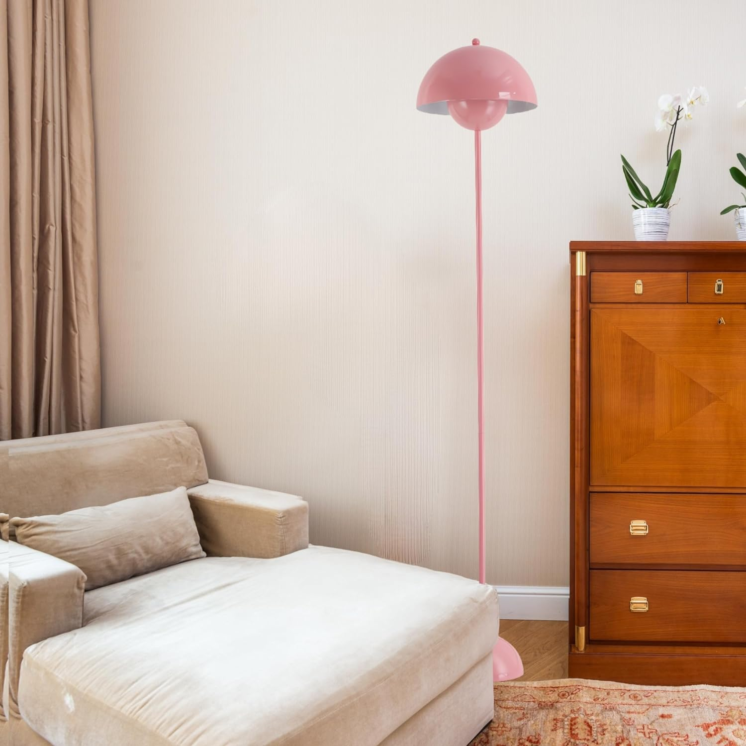 Lámpara de pie rosa con pantalla de hongo, junto a sofá beige y mueble de madera, en habitación con paredes blancas.