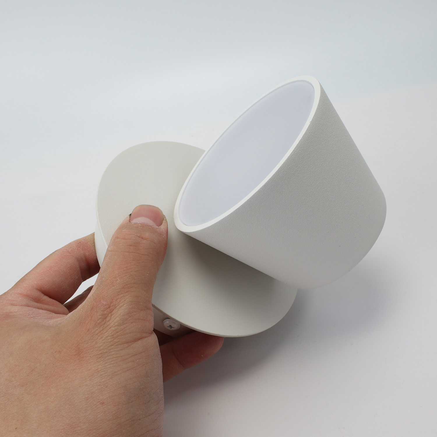 Una lámpara de pared blanca con una luz giratoria en forma de cono. Una mano gira la luz.