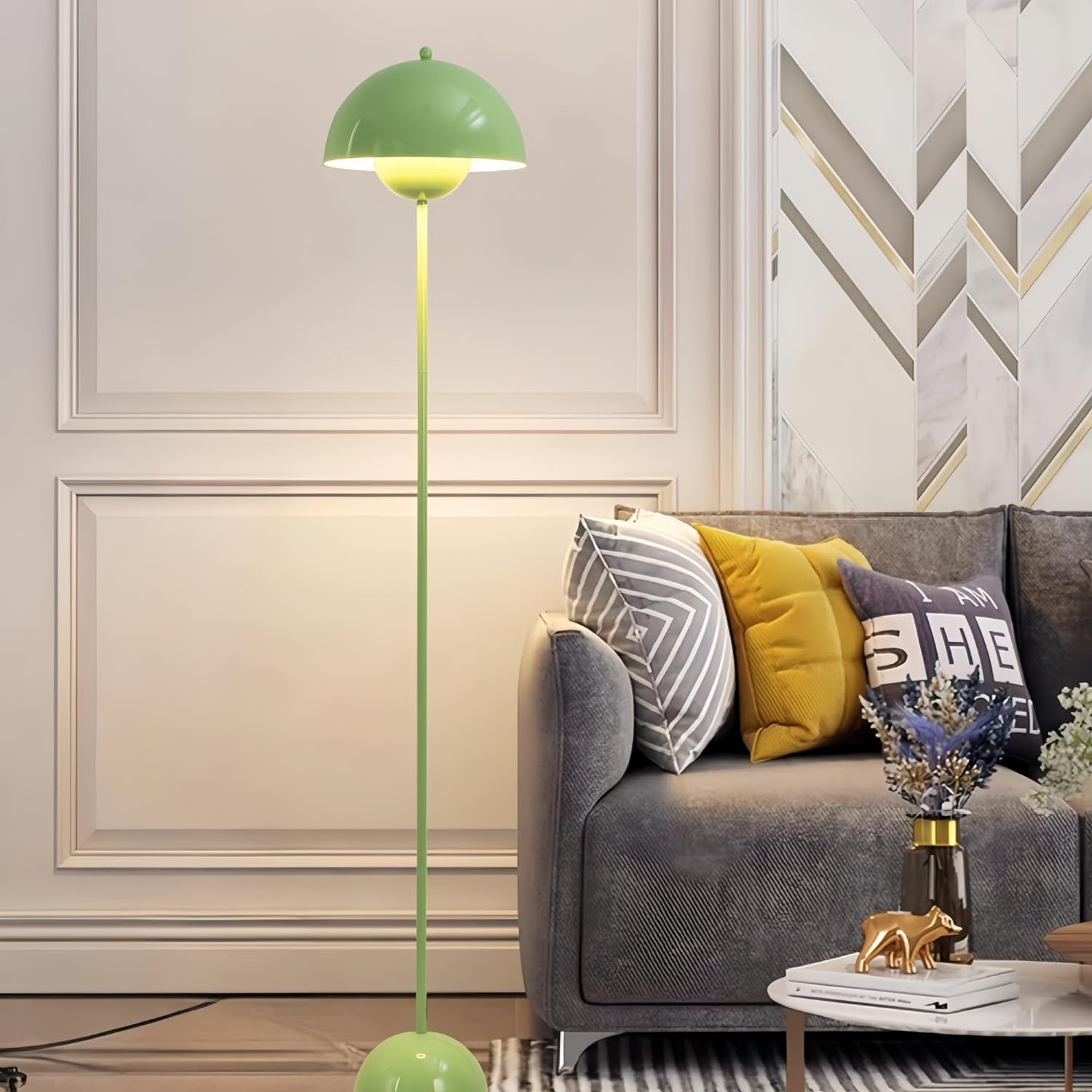 Una lámpara de pie verde en una sala de estar, con un sofá, almohadas y objetos decorativos en una mesa auxiliar.