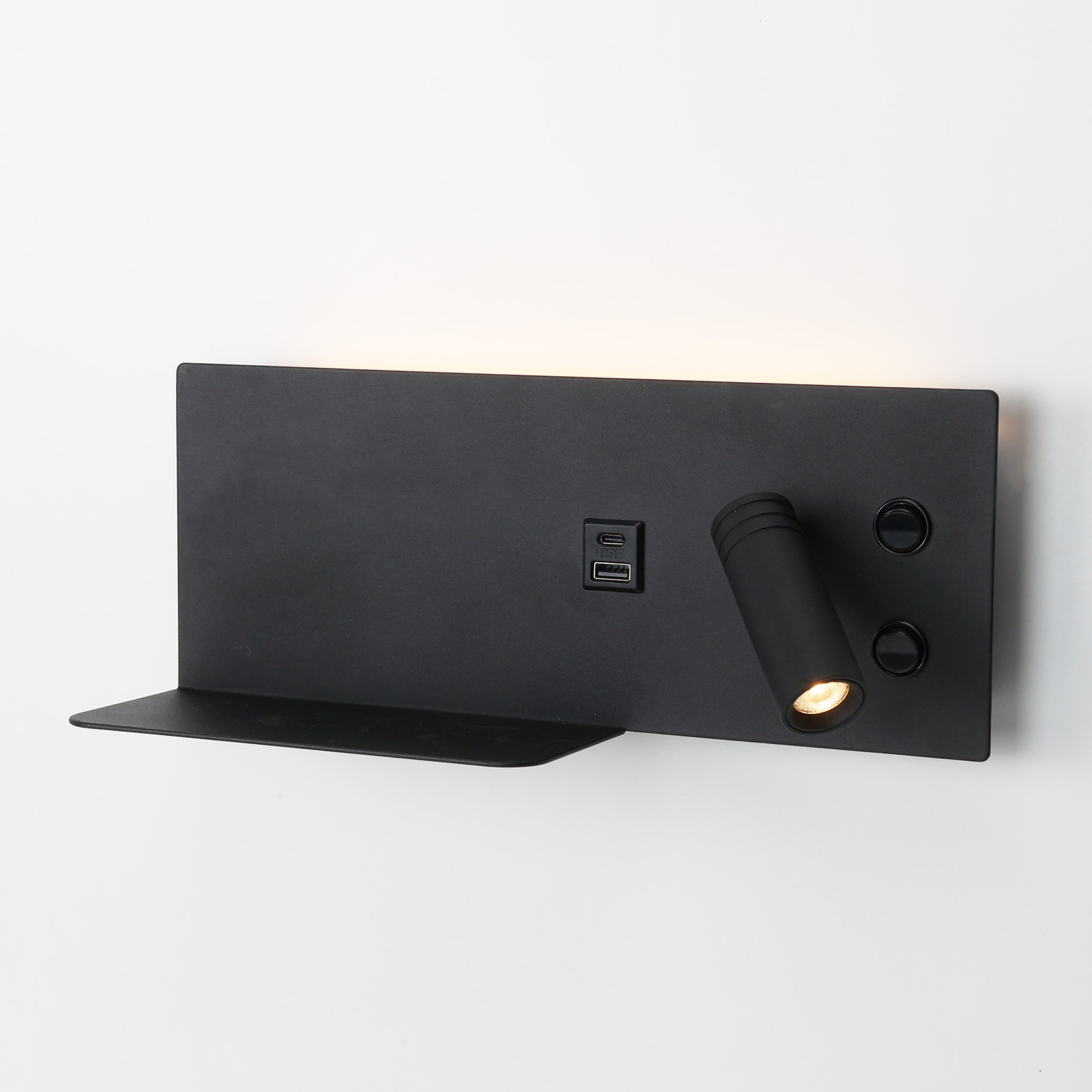 Una lámpara de pared negra con un estante, dos puertos USB y dos botones. La lámpara está en la pared.